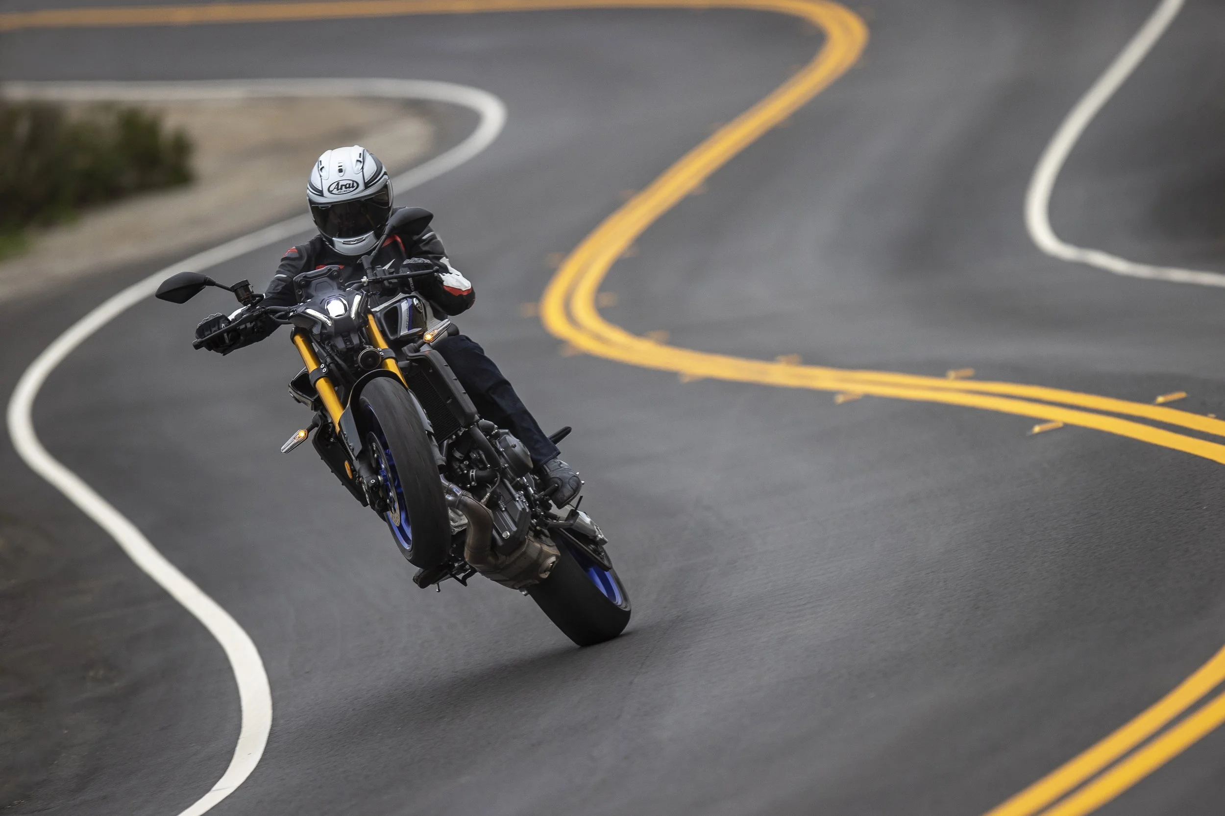 A motorcyclist wearing a helmet and riding gear is performing a sharp turn on a winding mountain road with yellow and white lines.