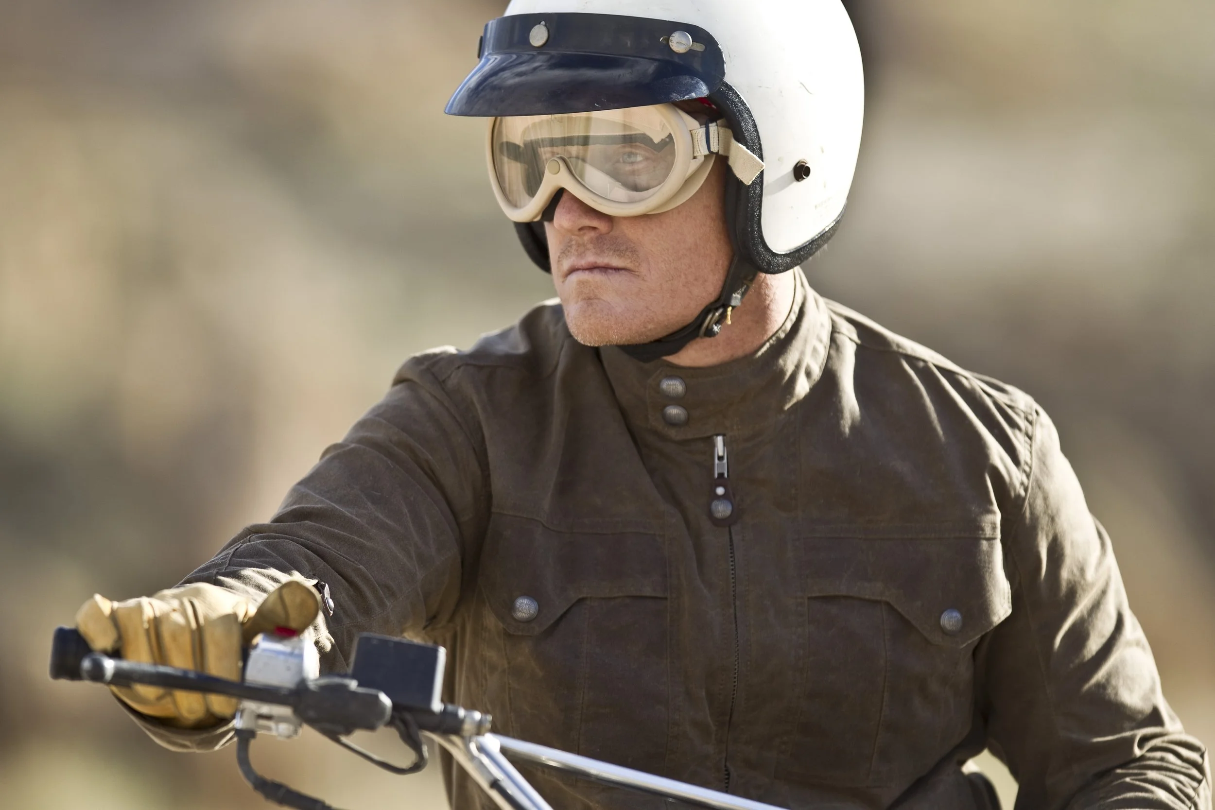 A man wearing a motorcycle helmet and goggles, riding a bicycle with a focused expression.