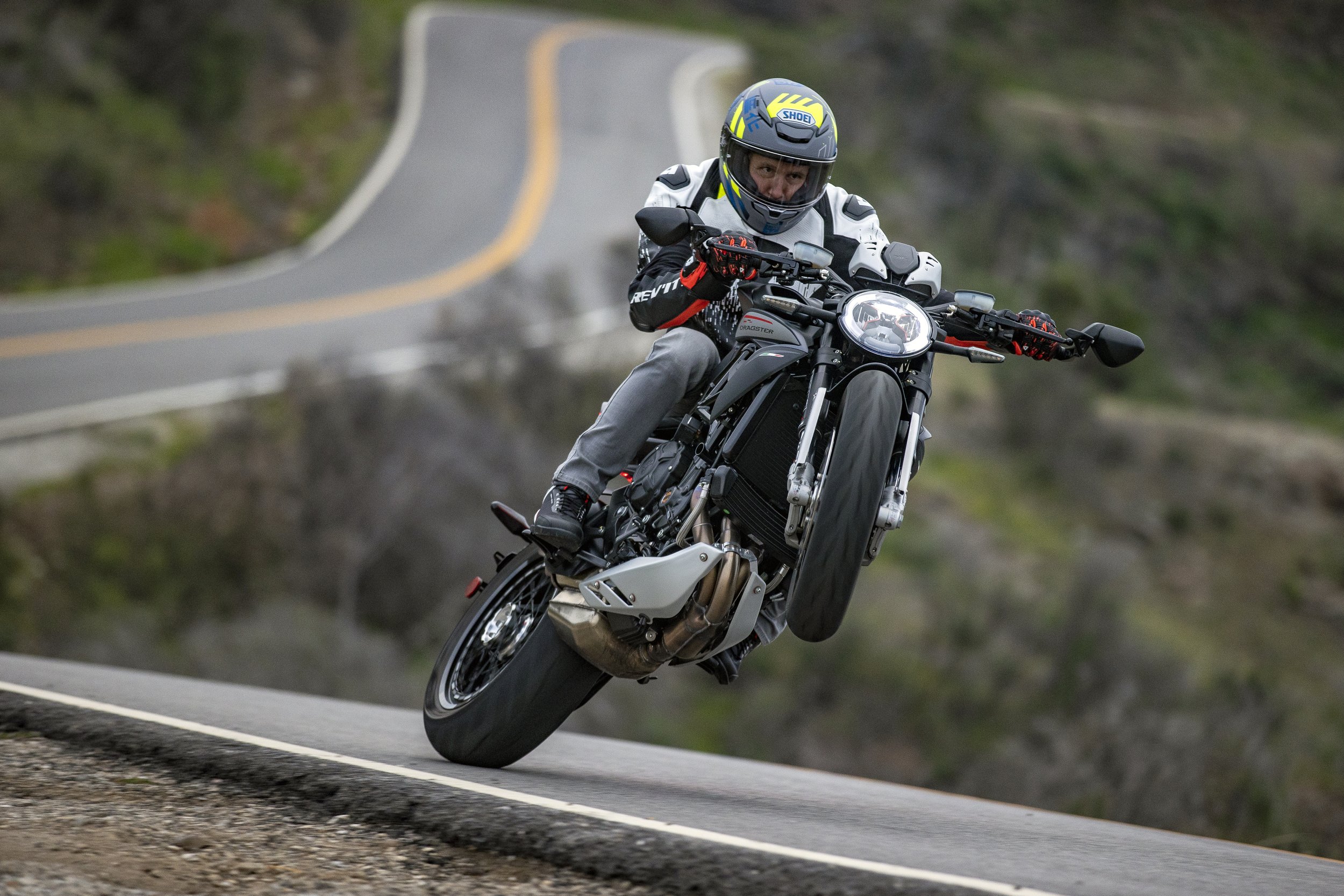 A person wearing a helmet and motorcycle gear riding a black motorcycle on a winding road.
