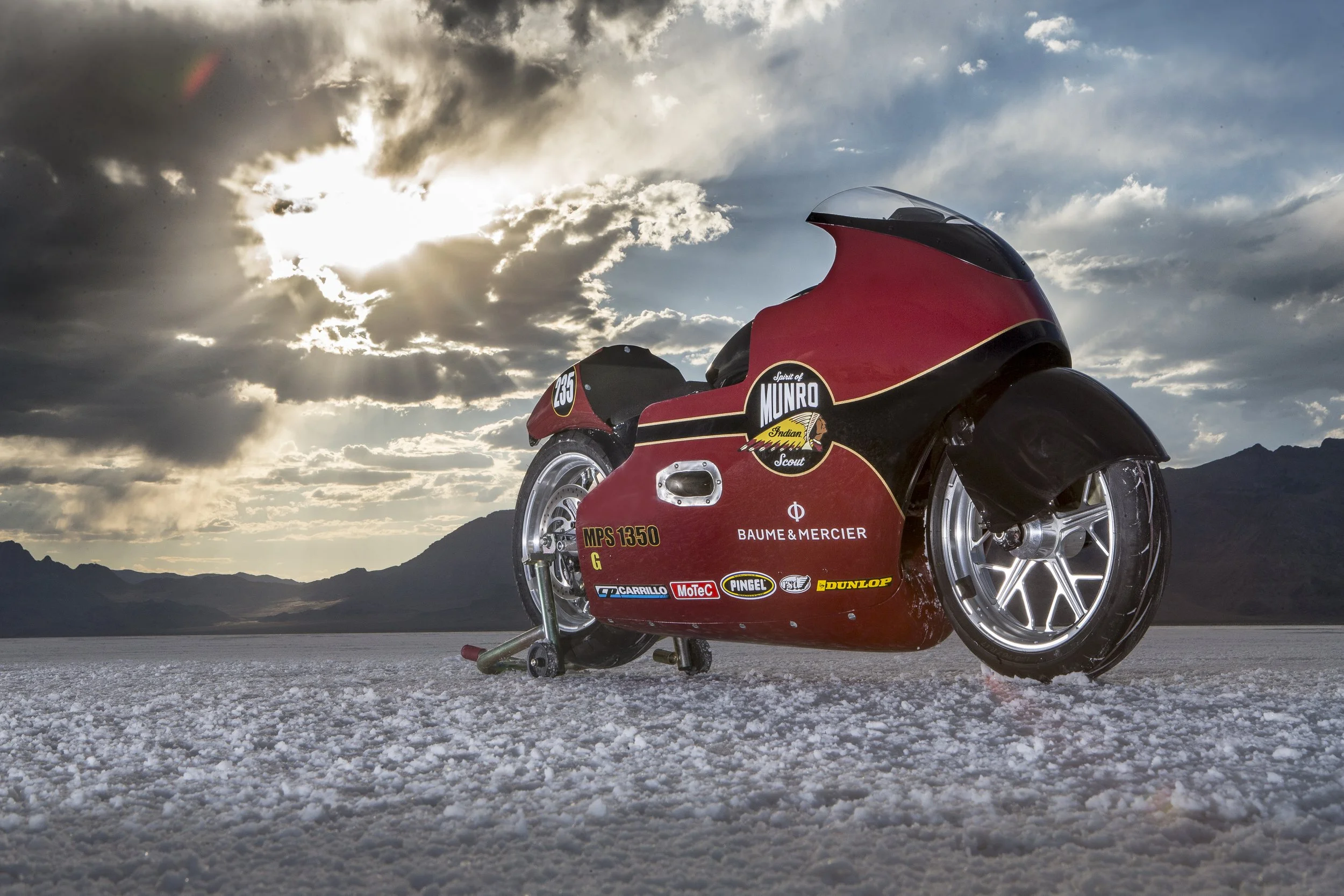 A red racing motorcycle with sponsor stickers parked on a salt flat during a cloudy day.