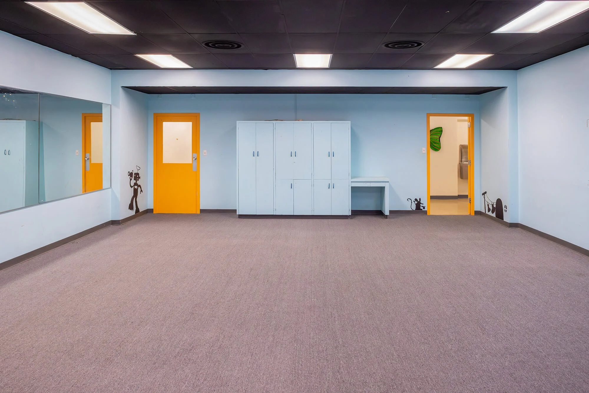 Empty room with light blue walls, orange doors, white lockers, and wall decals.
