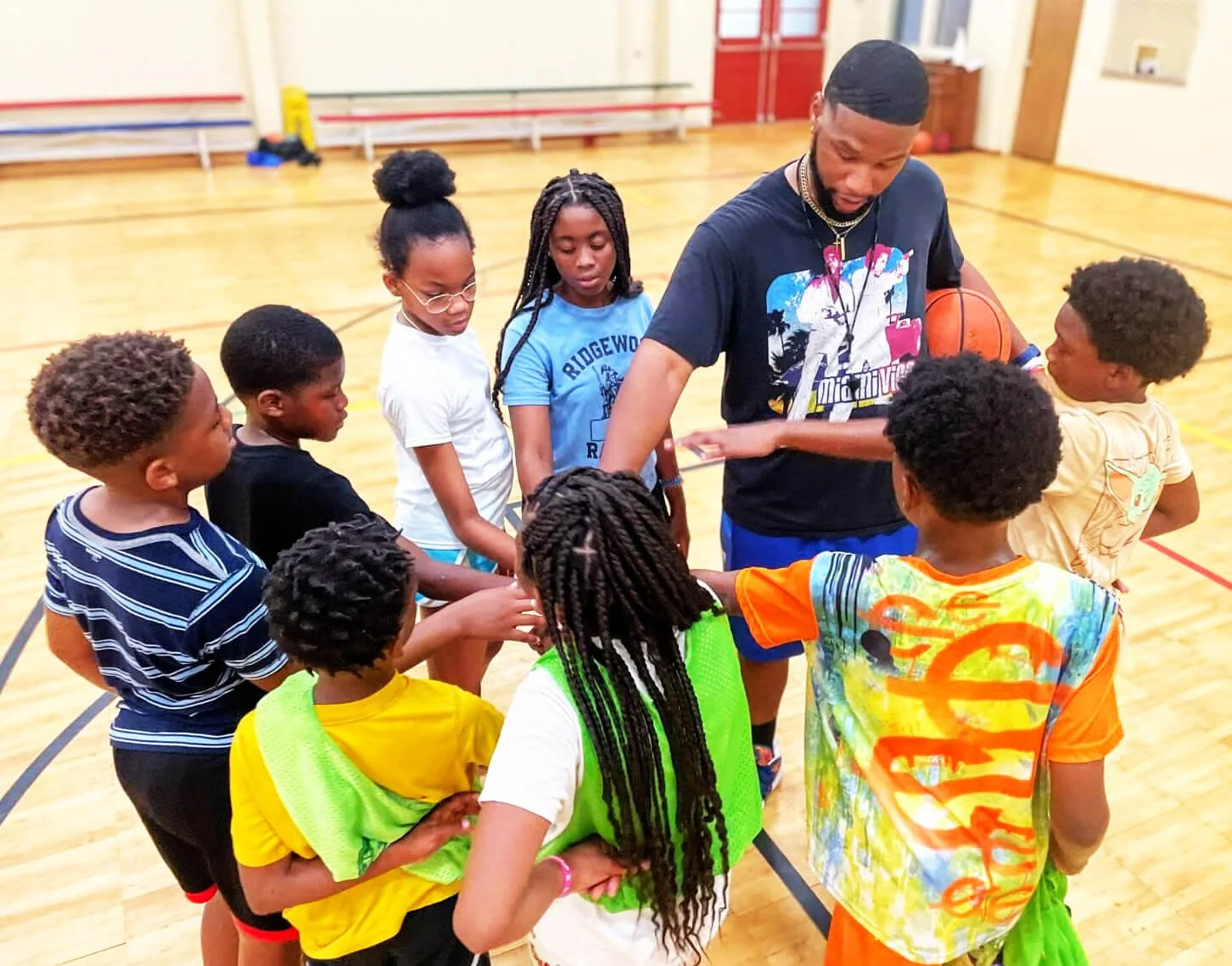 A basketball coach and a group of young children in a gymnasium, huddled and engaging in a team-building activity.