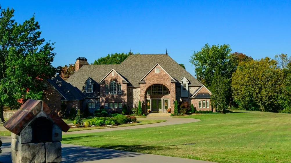 Large brick house with a well-maintained front lawn and trees on a sunny day.