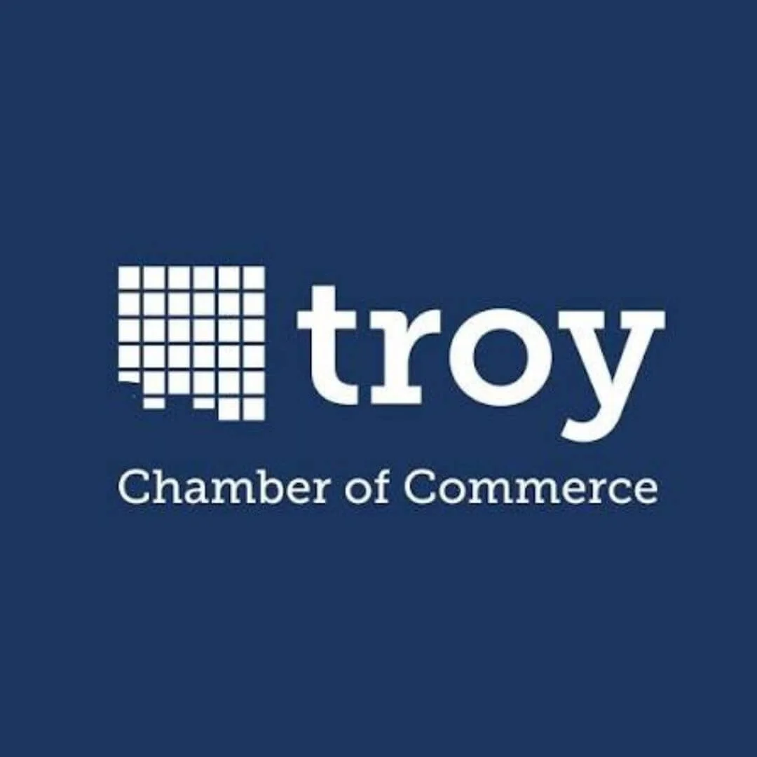 Troy Chamber of Commerce logo, with a mosaic of squares forming a stylized 'T' to the left of the text, on a dark blue background.