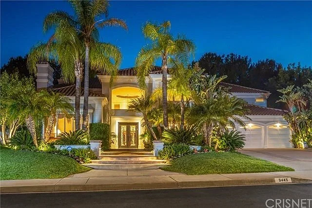 Luxury house with tropical landscaping, palm trees, and outdoor lighting at night.