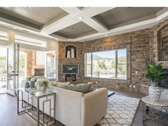 Living room with brick walls, large windows, a sectional sofa, fireplace, and decorative plants.