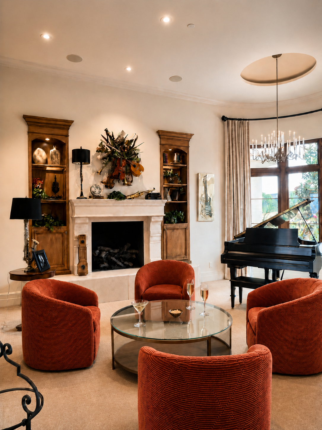Living room with a white fireplace, wooden shelves, a black grand piano, four red upholstered chairs around a glass coffee table with drinks, a chandelier, and a window with curtains.