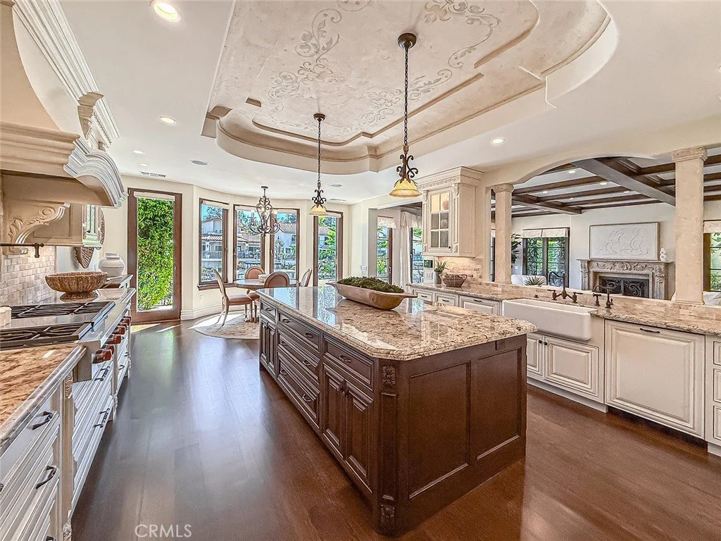 Spacious kitchen with white cabinets, granite countertops, and a kitchen island with dark wood finish. Features a farmhouse sink, stainless steel appliances, and a dining area with a round table by large windows.