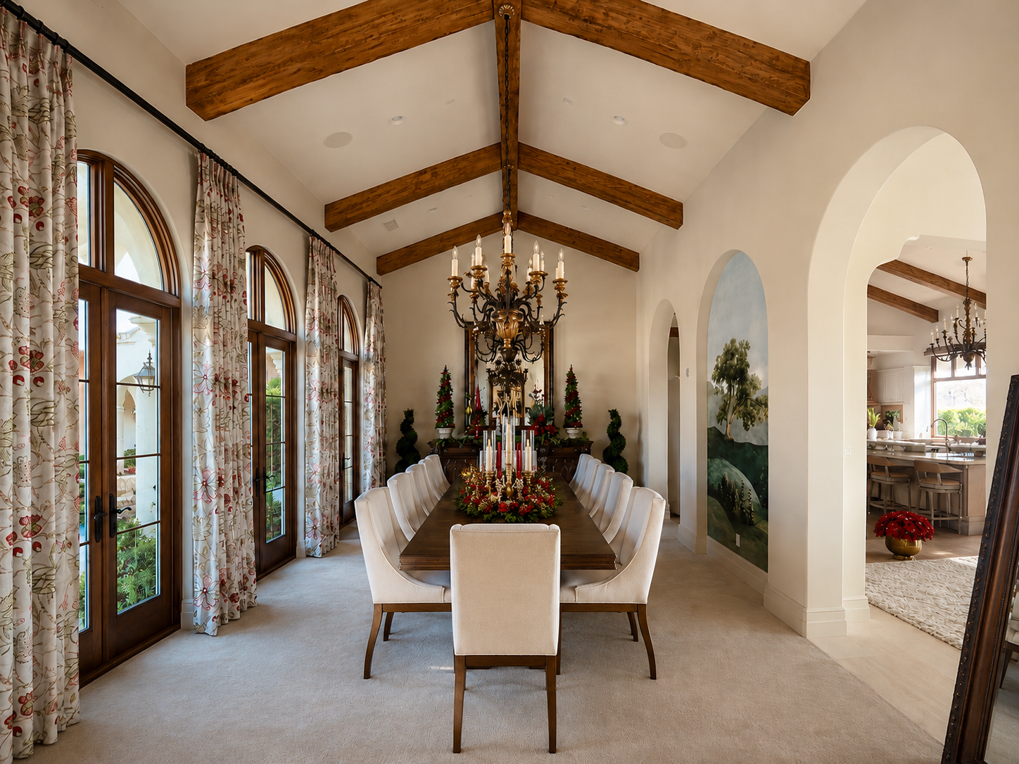 Elegant dining room with arched windows, floral curtains, a long wooden table decorated for Christmas with candles and poinsettias, and a large chandelier hanging from a vaulted ceiling with wooden beams.