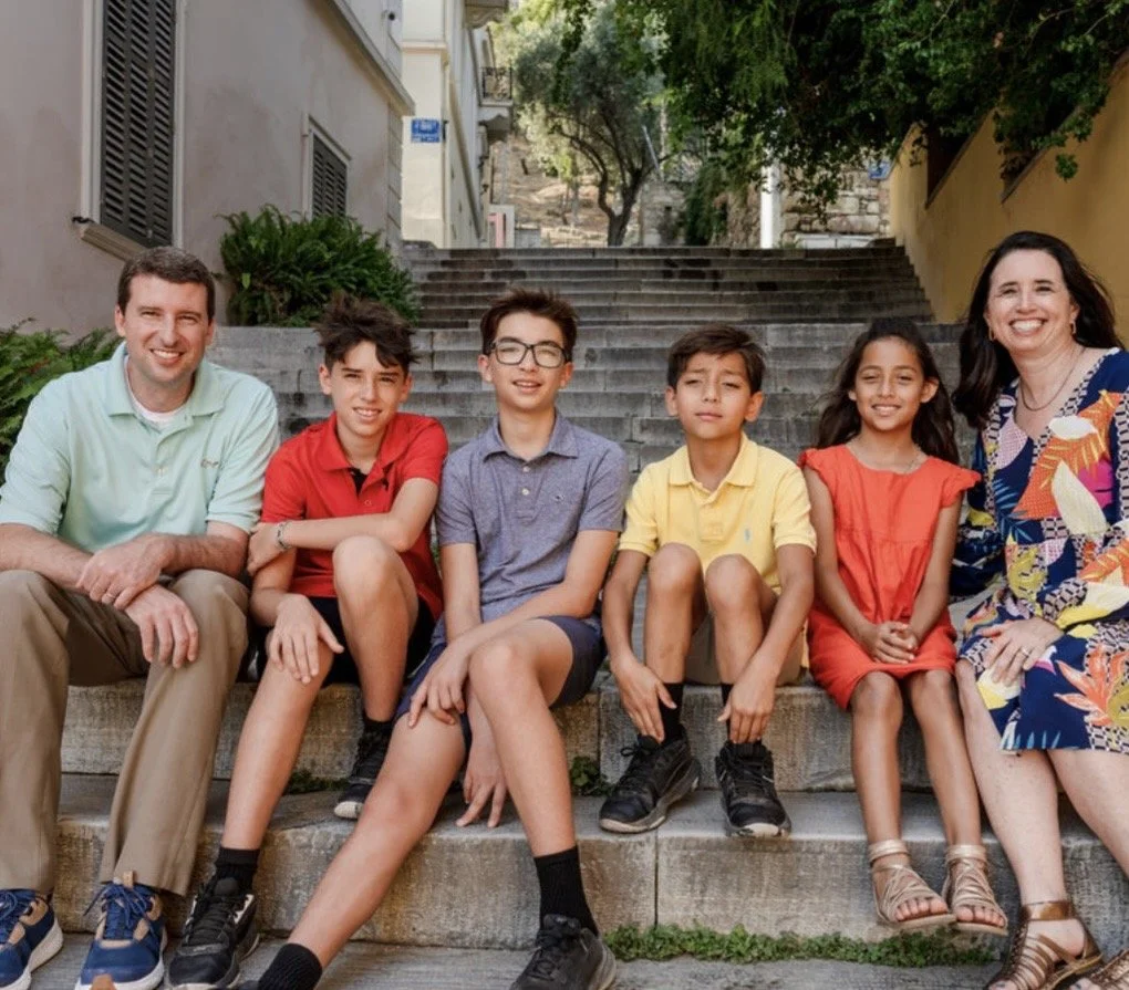 The Johnson family - A group of four children and two adults sitting on outdoor steps, smiling at the camera, with buildings and trees in the background.