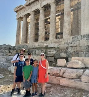 Group of five children and teenagers standing in front of the Parthenon in Athens, Greece, on a sunny day.