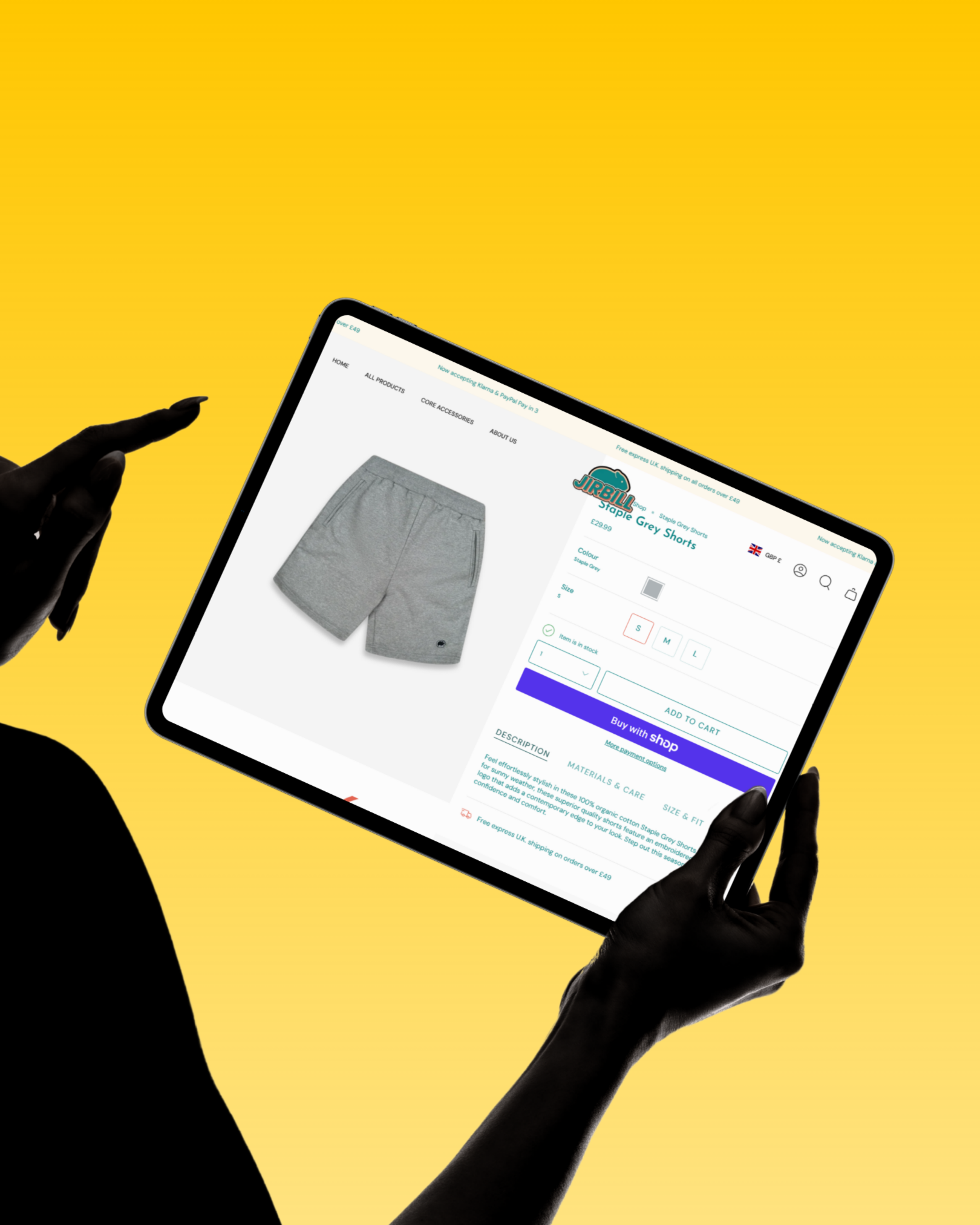 A person with black skin is holding a tablet showing an online store webpage for gray shorts, with a yellow background.