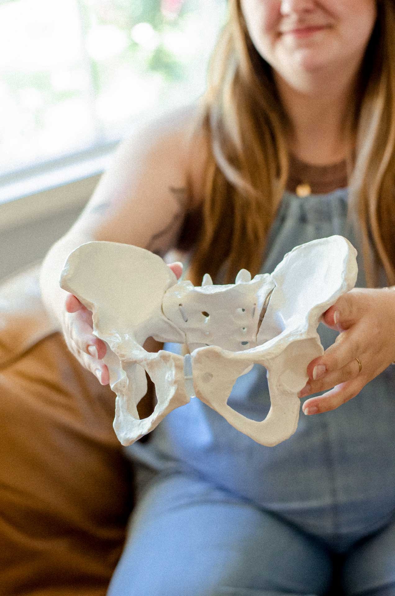 A woman holding a detailed model of a human pelvis or hip bone.
