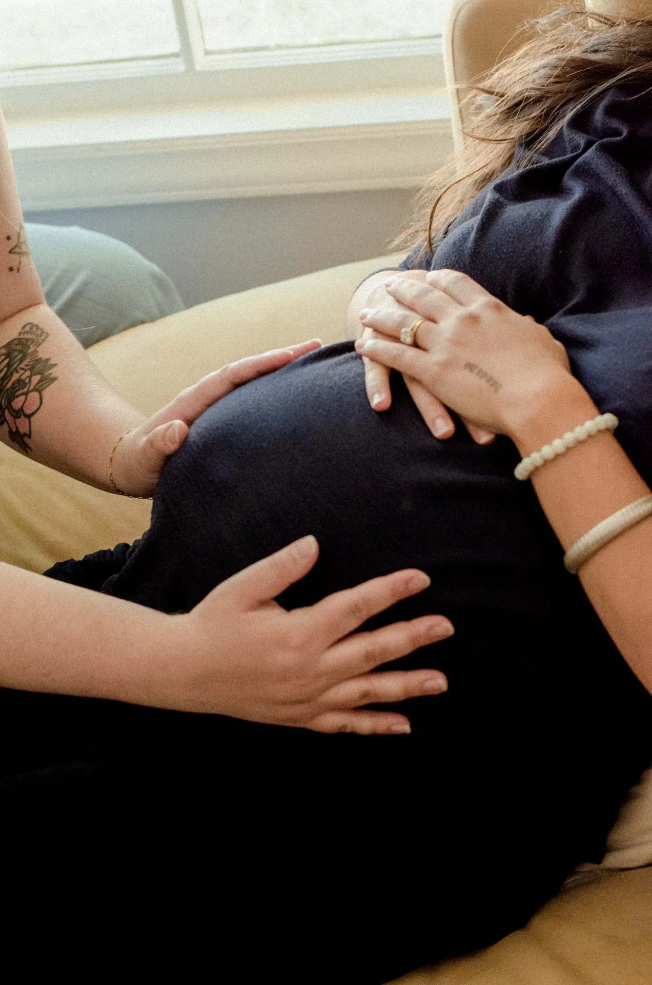 Multiple hands gently touching a pregnant woman's belly in a cozy, softly lit room.