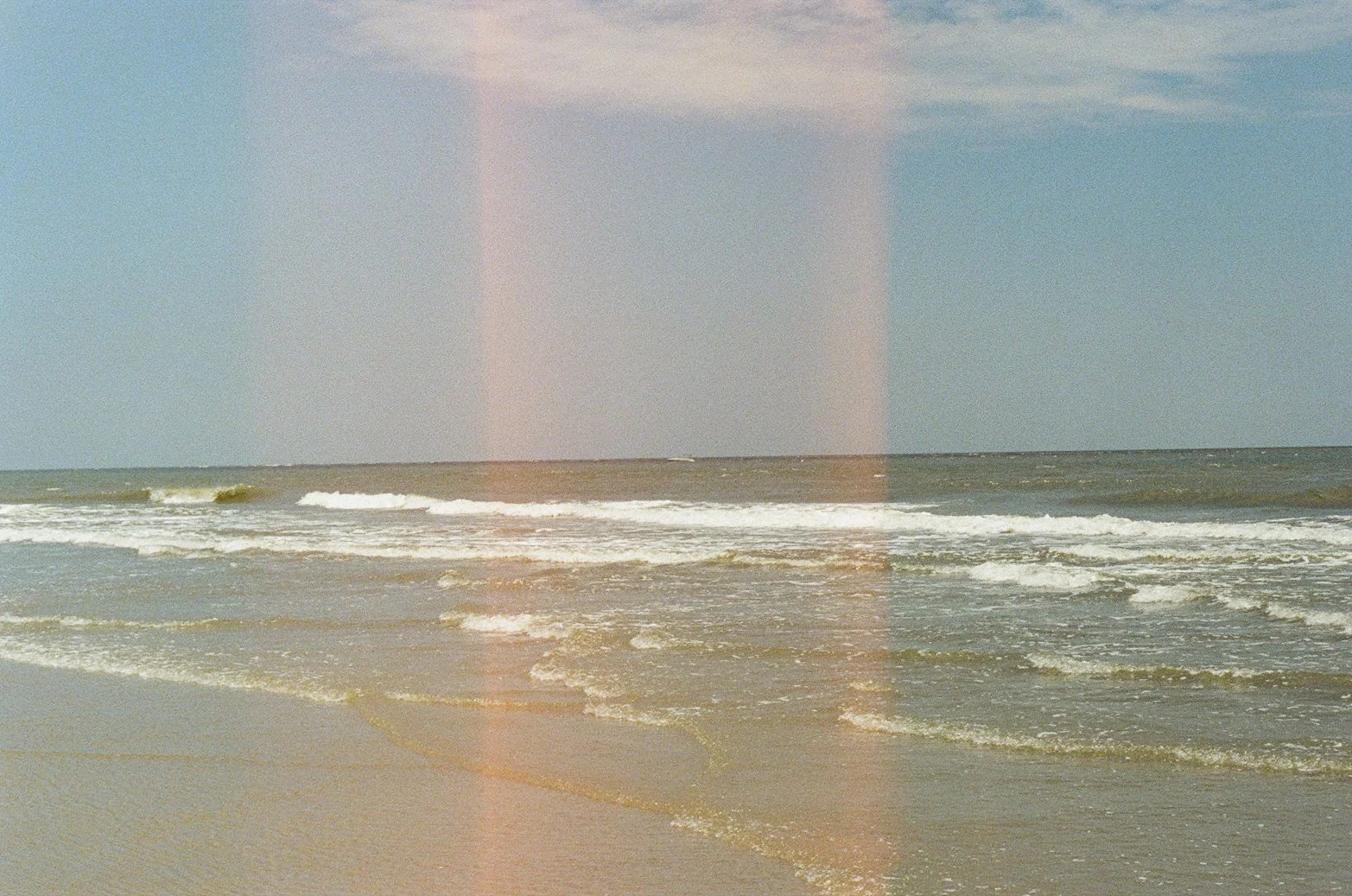 A calm ocean scene with gentle waves rolling onto a sandy beach under a partly cloudy sky.