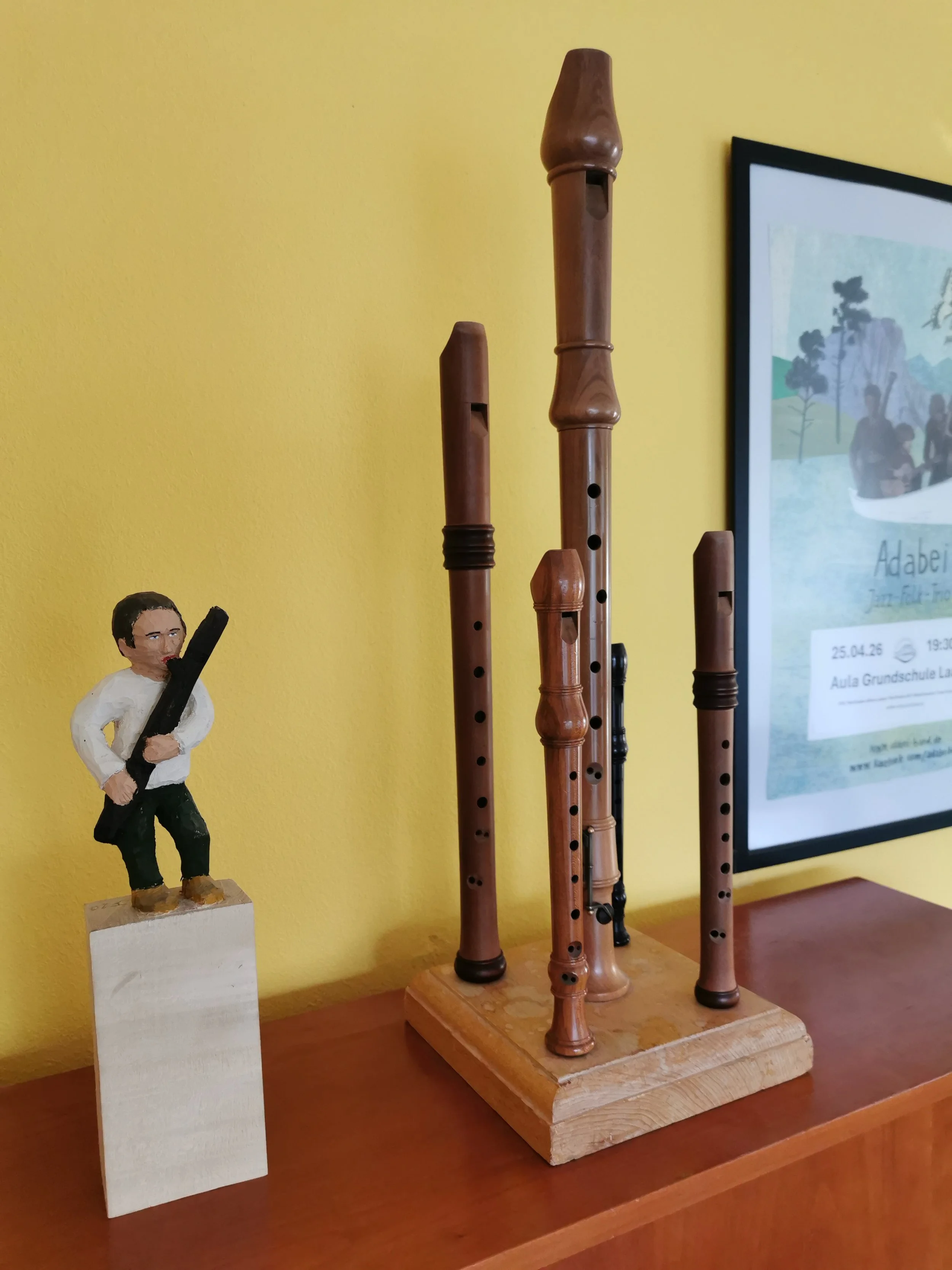 Holzblockflöten in verschiedenen Größen auf einem Klavier, daneben eine handgefertigte Figur eines Mannes mit einem Fagott in der Hand vor einem gelben Hintergrund.