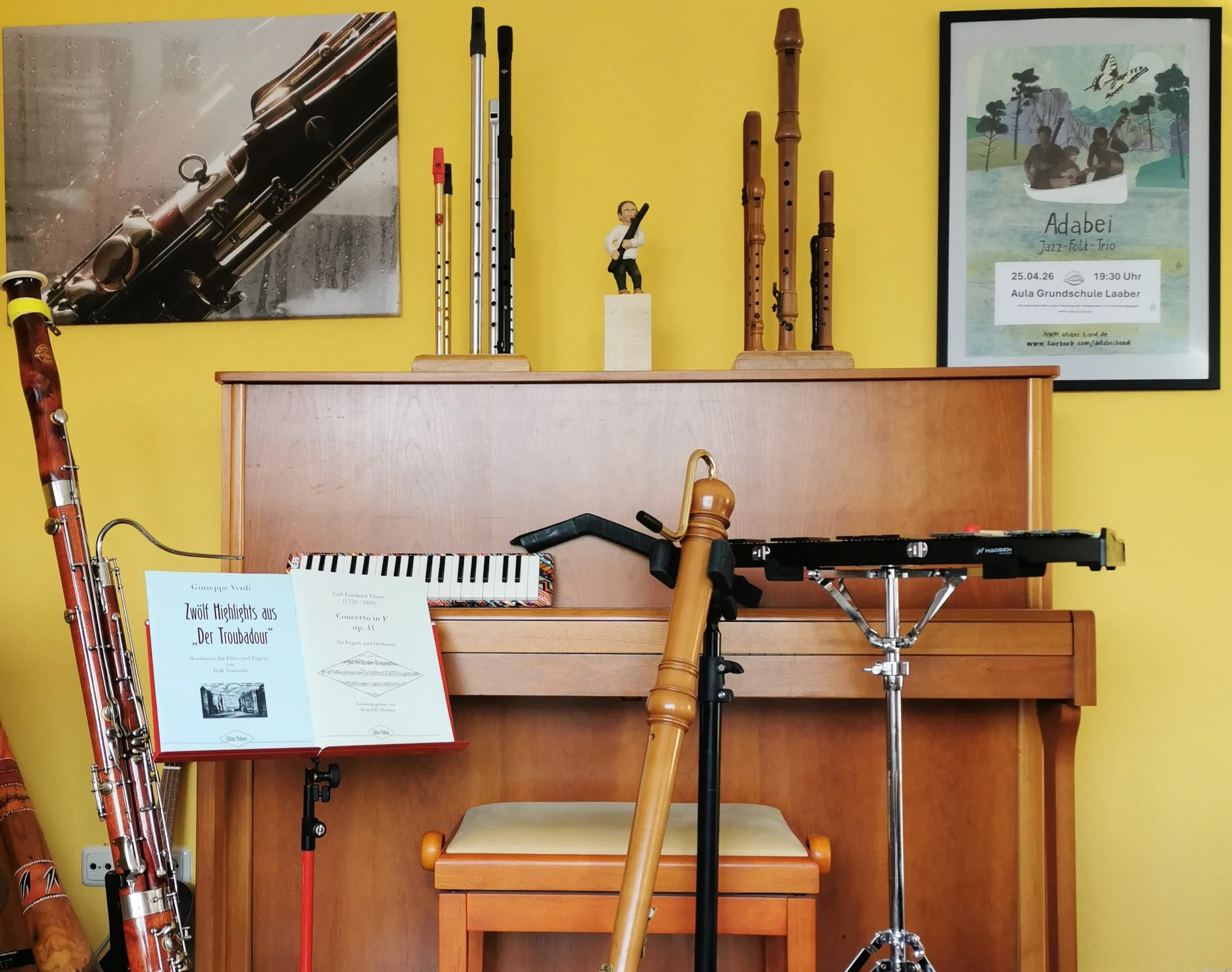 Musikinstrumente, darunter Flöten, ein Fagott, ein Klavier und ein Glockenspiel. Es gibt auch Noten und ein Poster für eine Veranstaltung.
