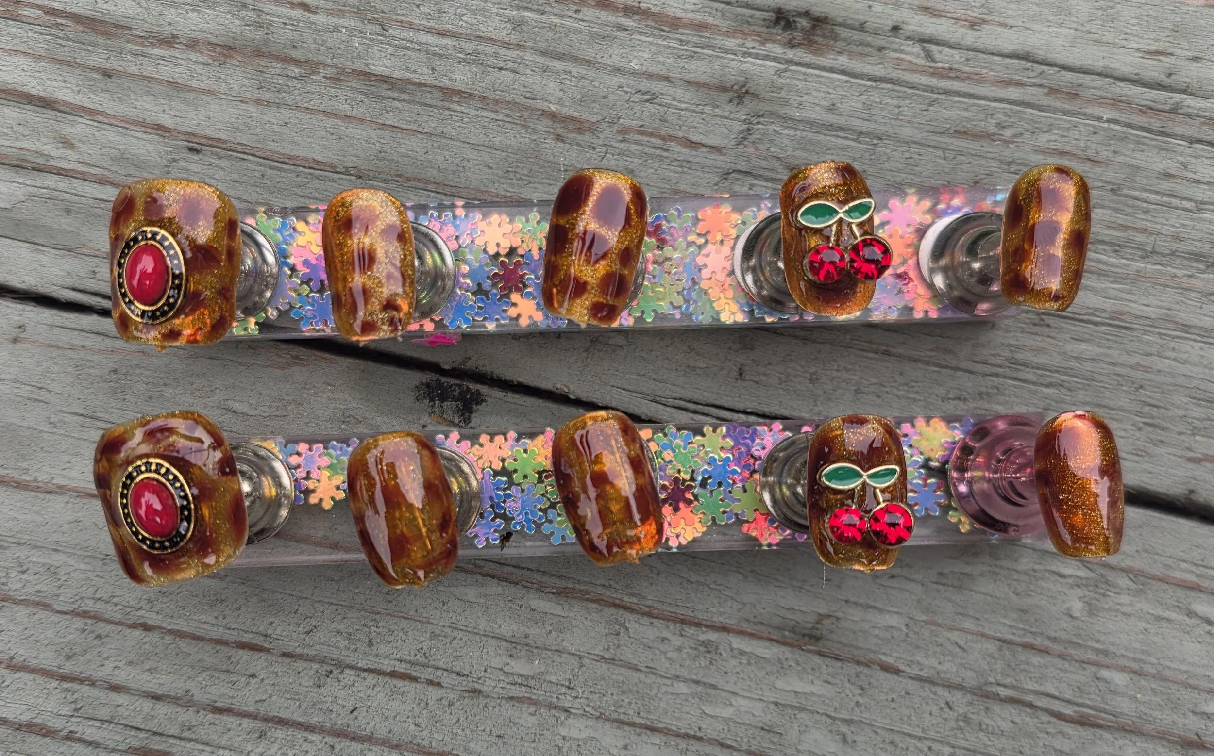Two decorative hairbands with large faux gem embellishments on a weathered wooden surface. The bands are covered with holographic, multicolored snowflake-patterned material.