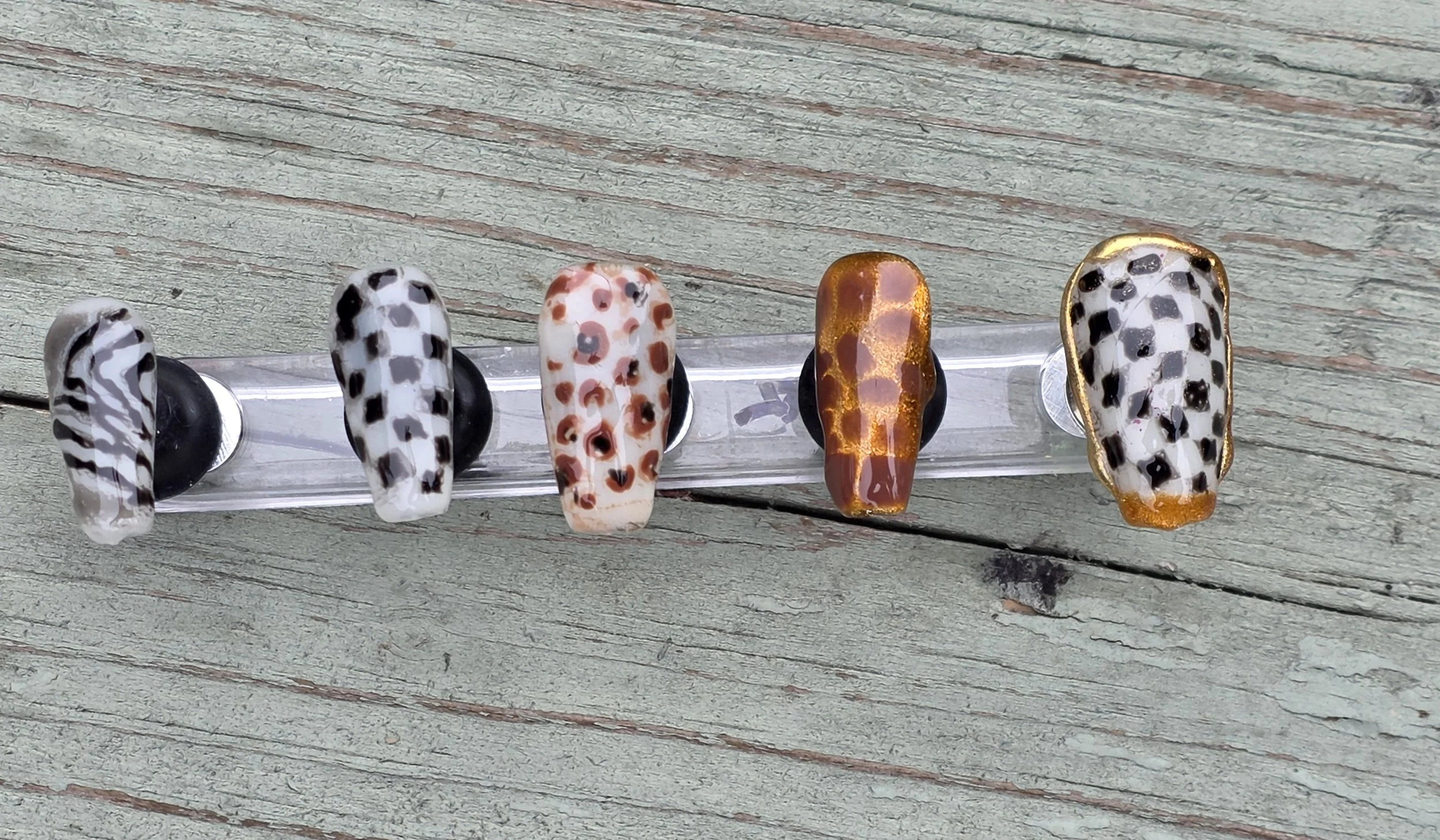 A clear plastic nail polish swatch stick with five different animal print nail designs, displayed on a wooden surface.