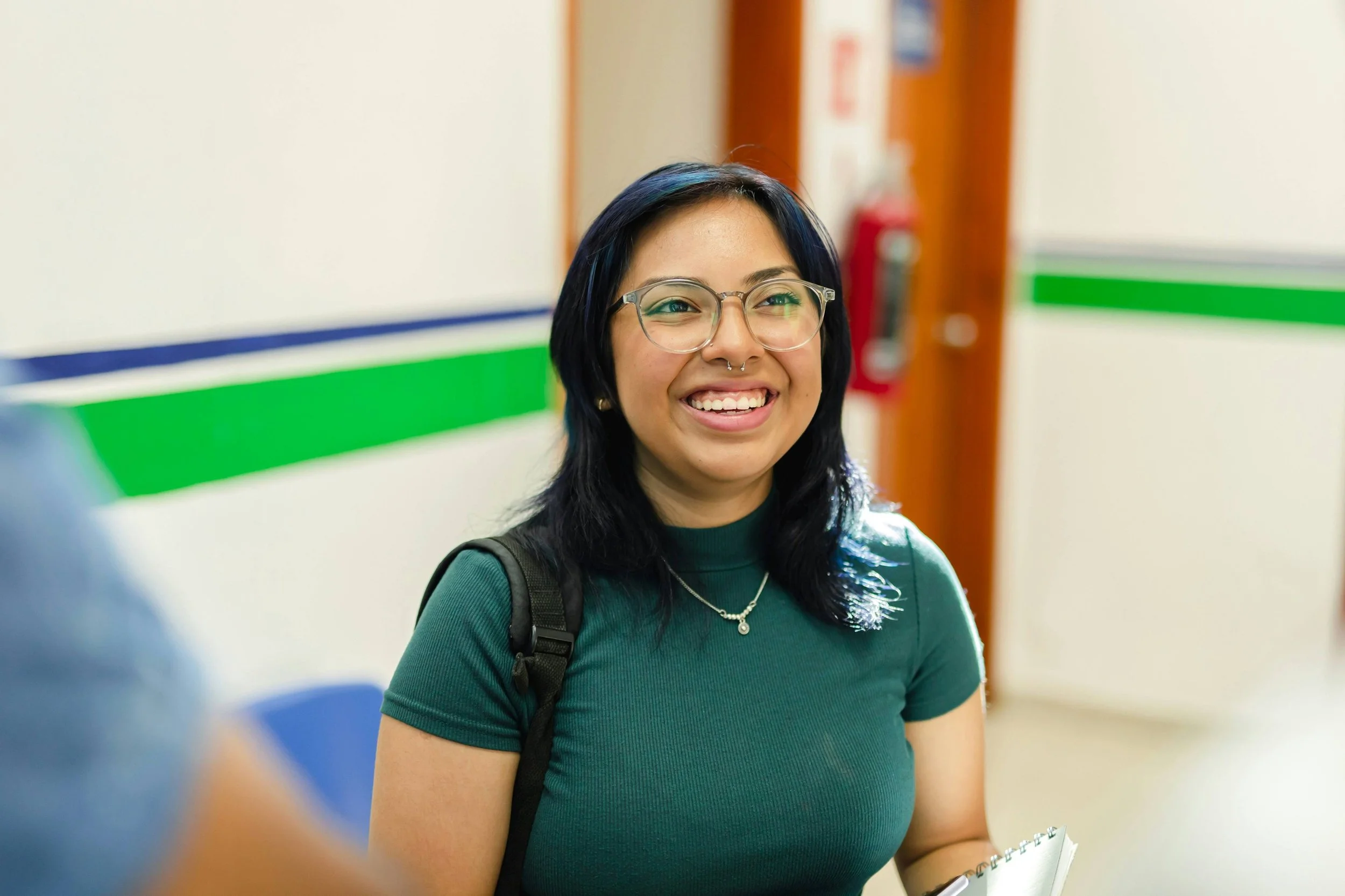Teenage Hispanic girl with glasses and a green shirt standing in a classroom and smiling-drop-shadow