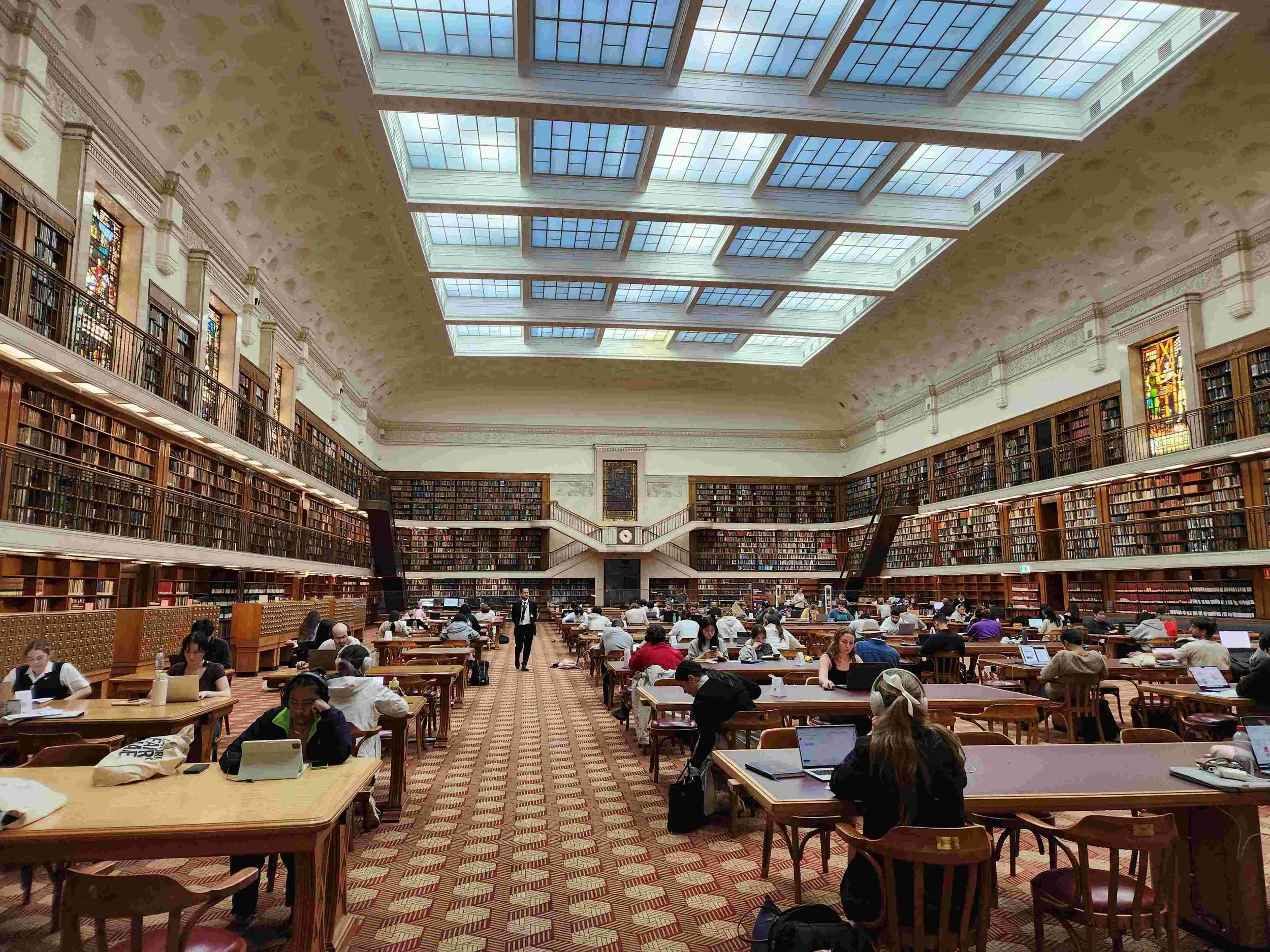 Large college library with students sitting at tables in the middle of the room-in teal card