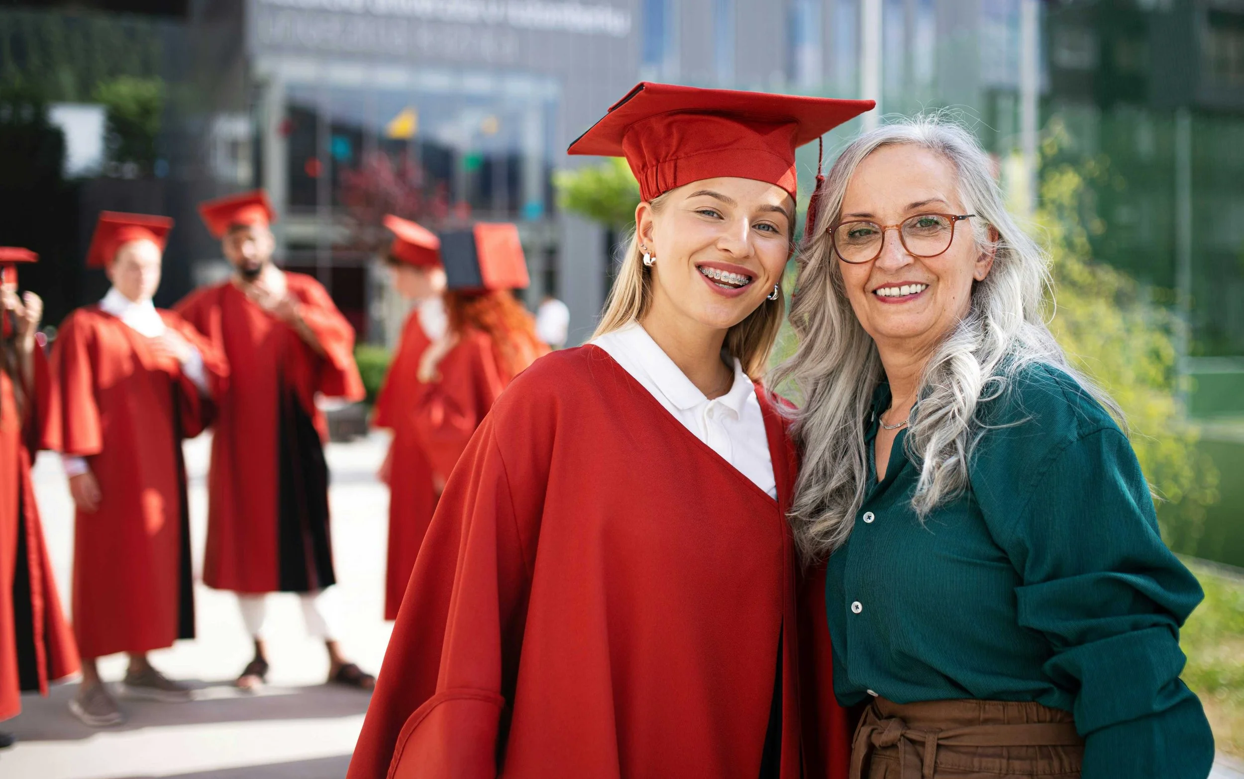 Teenage girl in red graduation robes smiling with her mother-drop-shadow