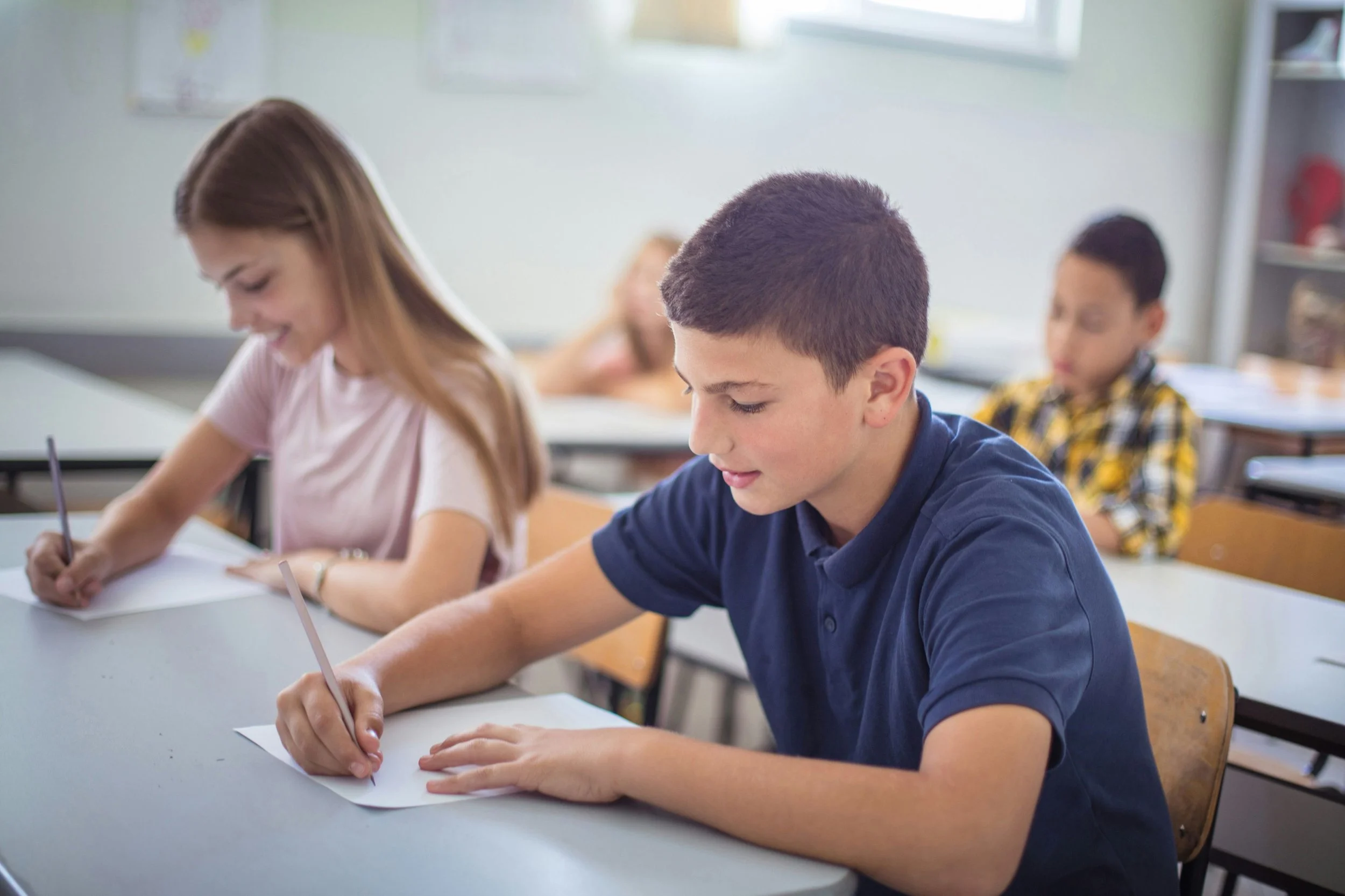 Students sitting at tables writing on a sheet of paper-in white card