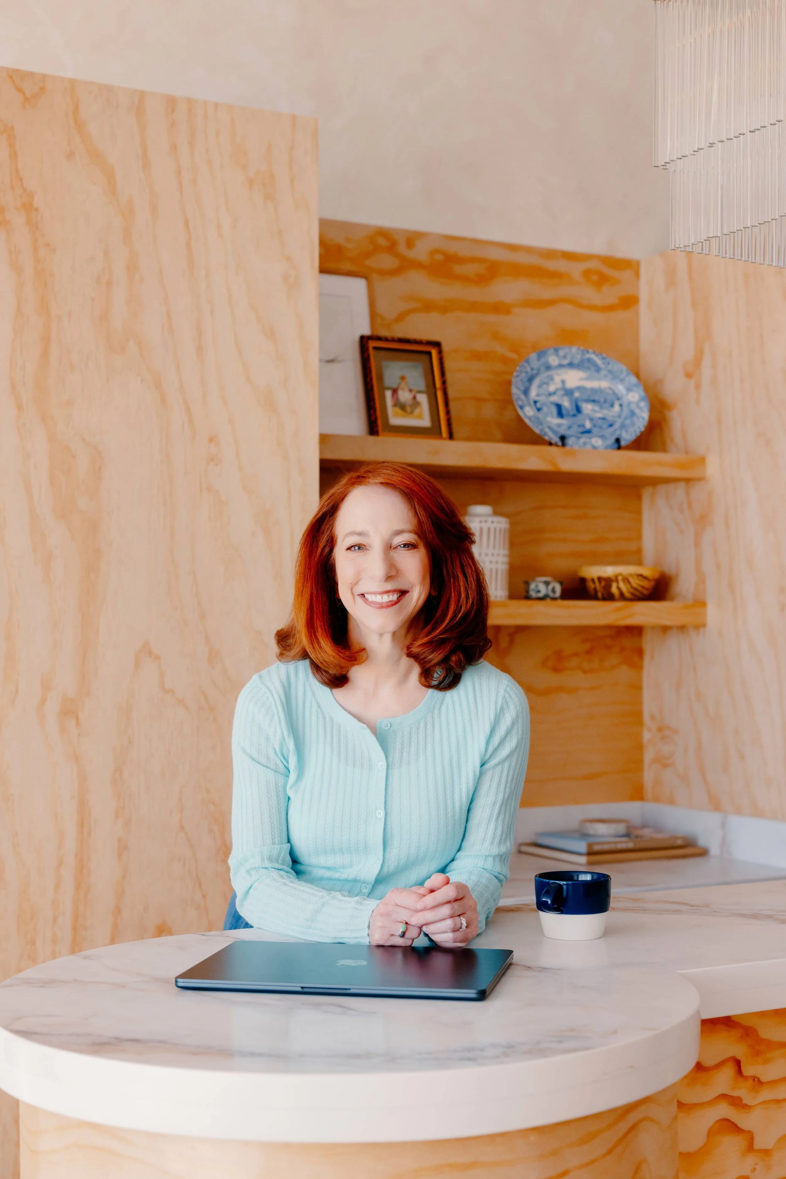 College admissions counselor Barbara Rifkind wearing a blue sweater and sitting at a table with wooden shelves behind her-drop-shadow