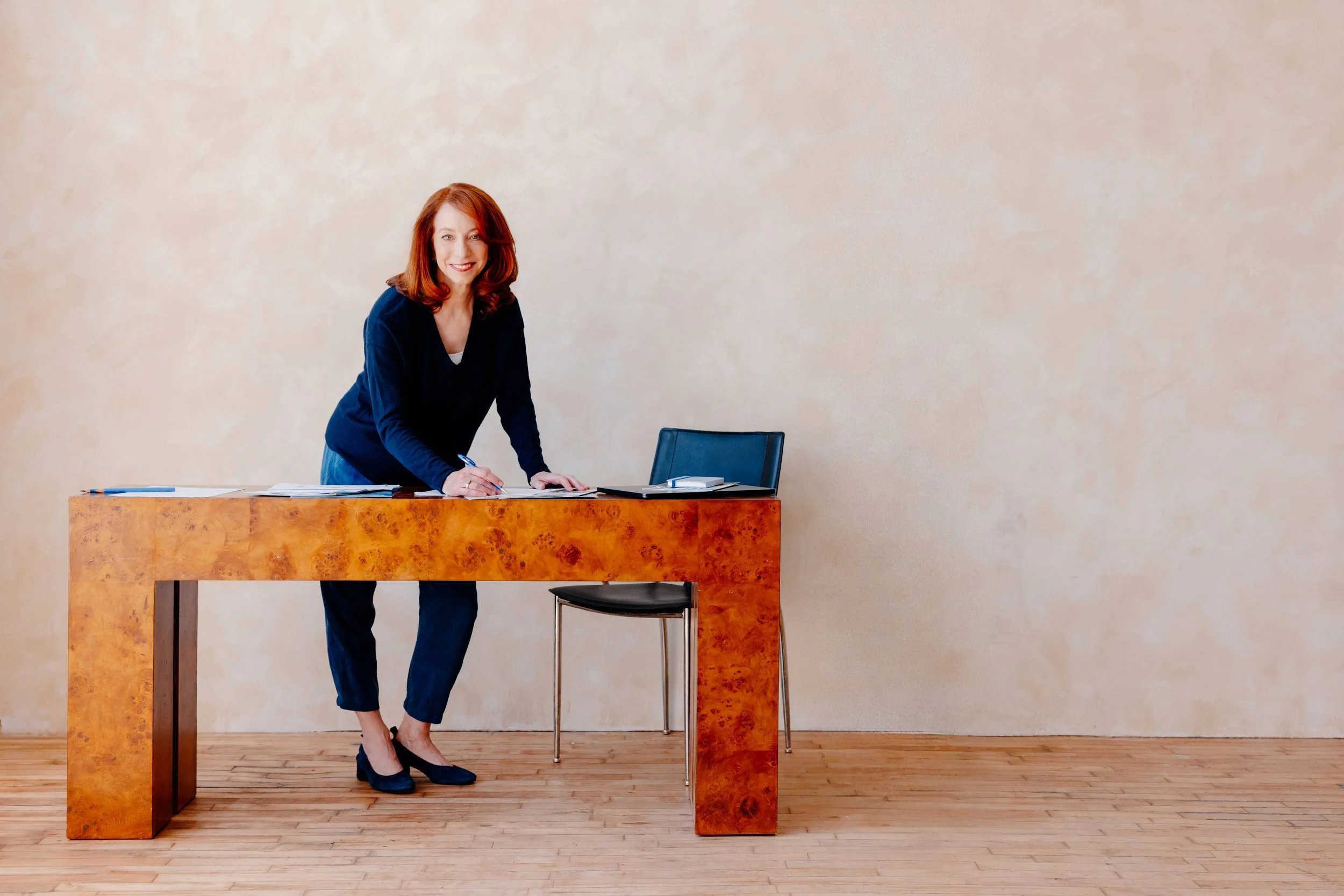 Barbara Rifkind standing behind a large wooden desk and writing on a piece of paper-drop-shadow