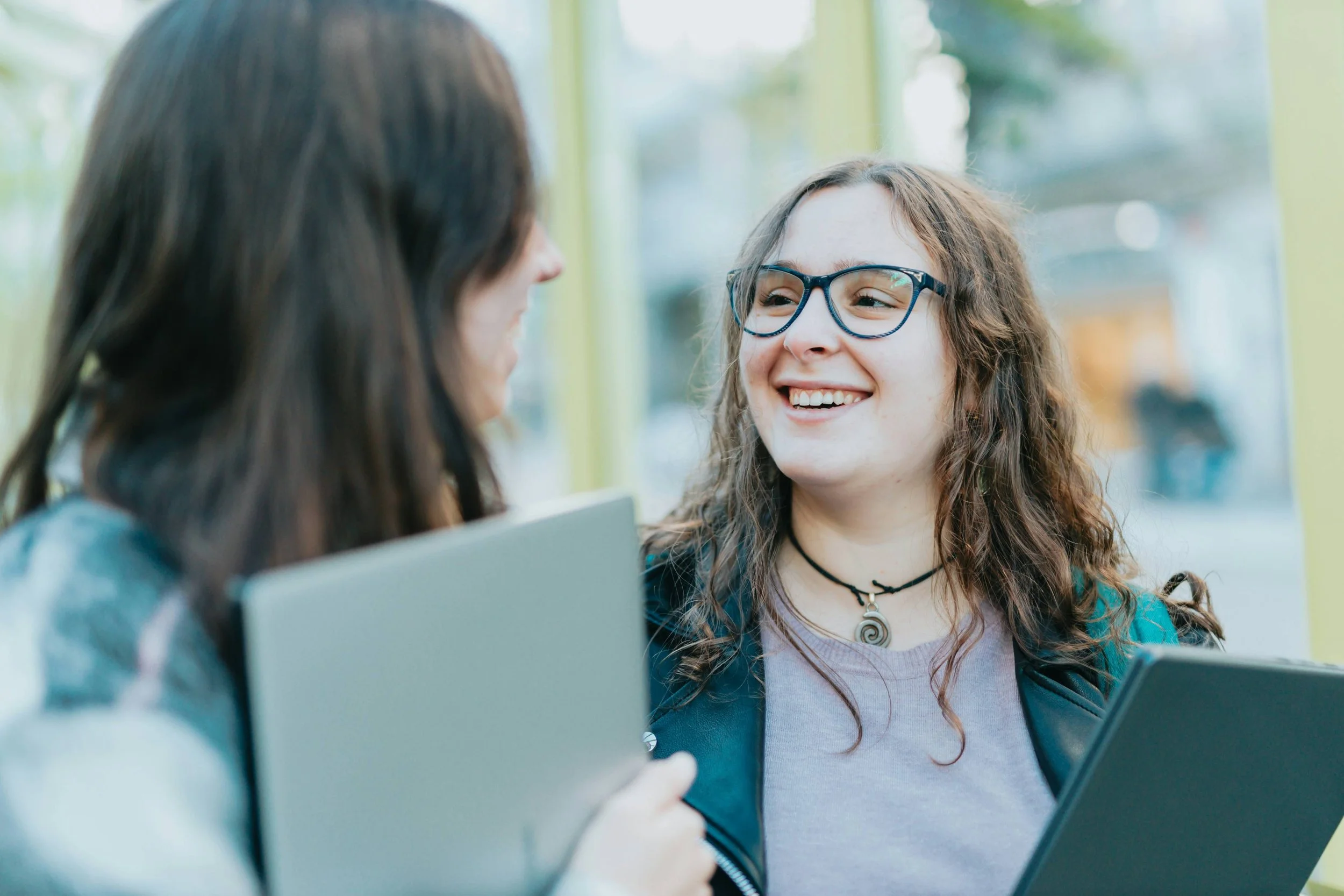 Two teenage girls holding laptops and laughing-in teal card