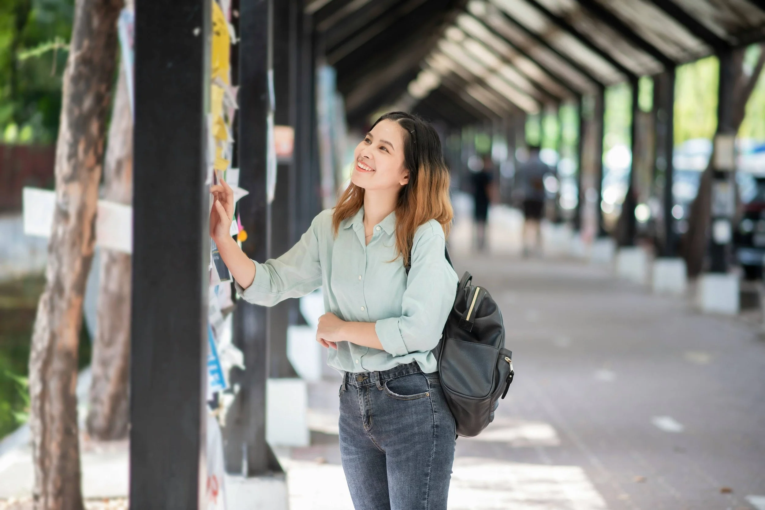 Teenage girl with a black backpack looking at a board of notices at a school-drop-shadow
