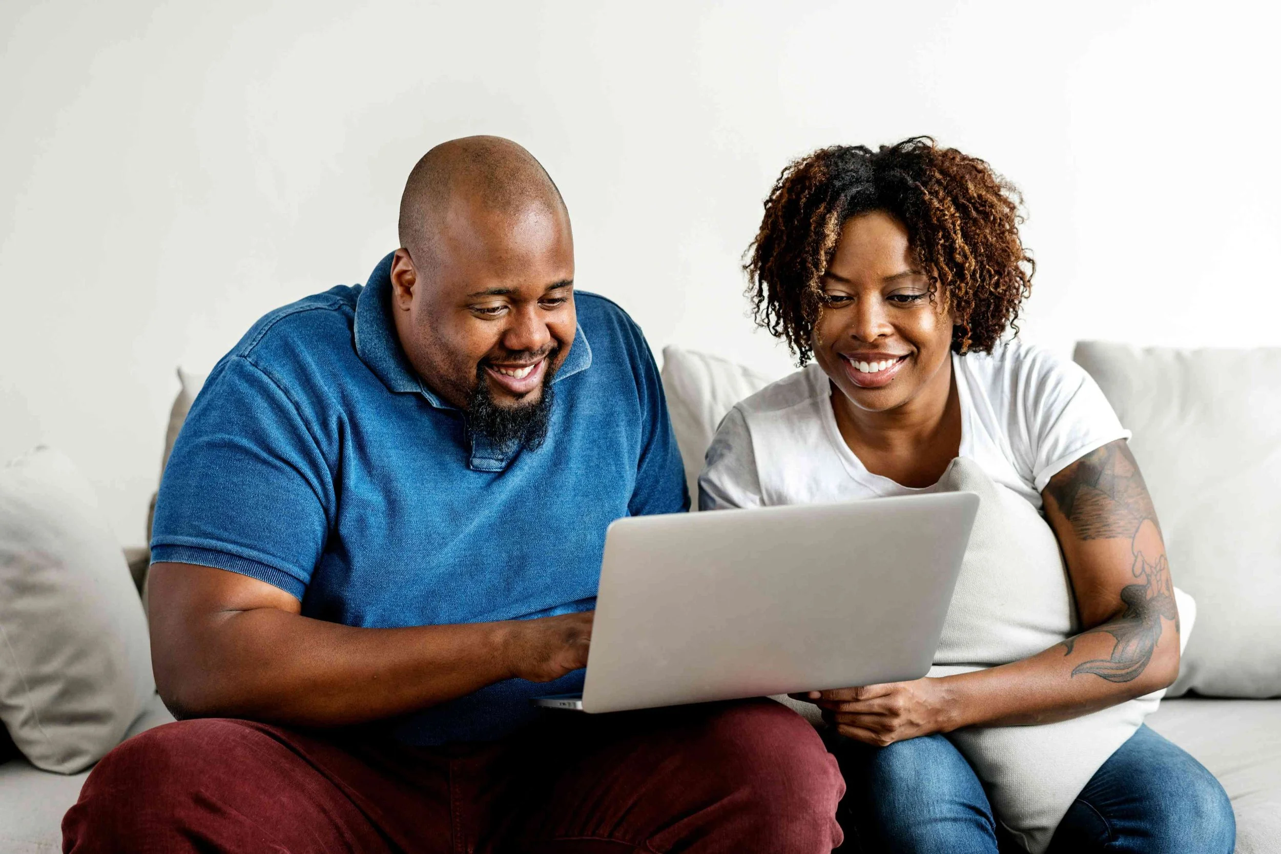 Black man and black woman sitting on a couch smiling at a laptop-drop-shadow