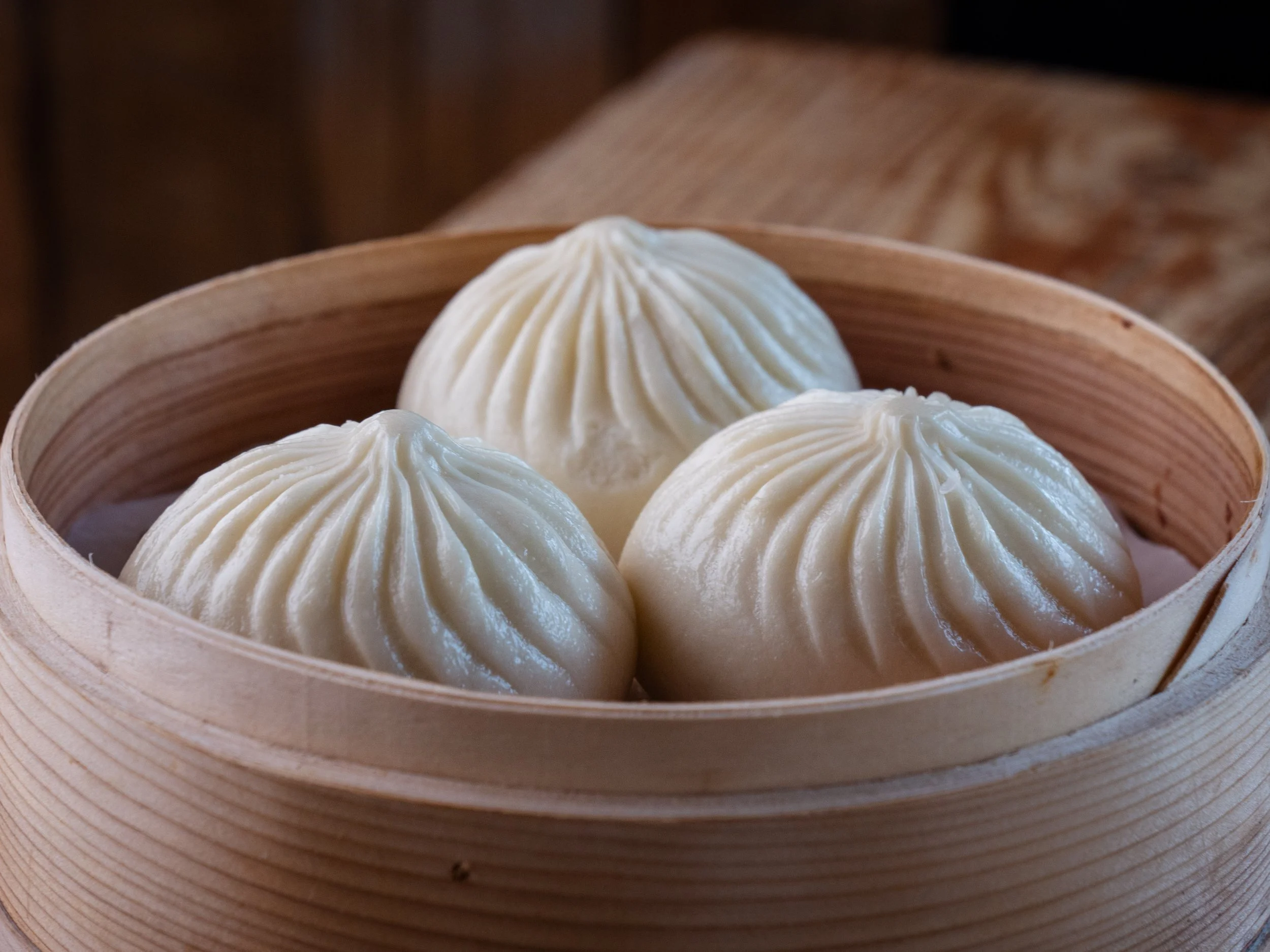 Three steamed dumplings in a round bamboo steamer basket.