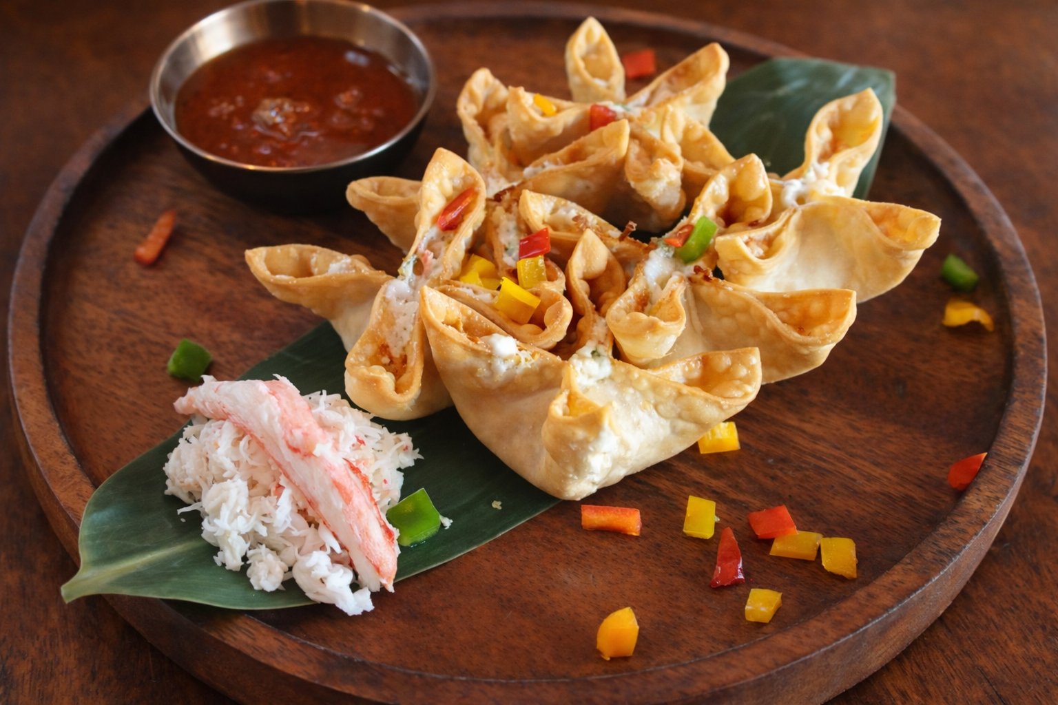 Crab rangoons on a wood plate with a small side of extra crab meat and dipping sauce for Nana's Dim Sum and Dumplings.