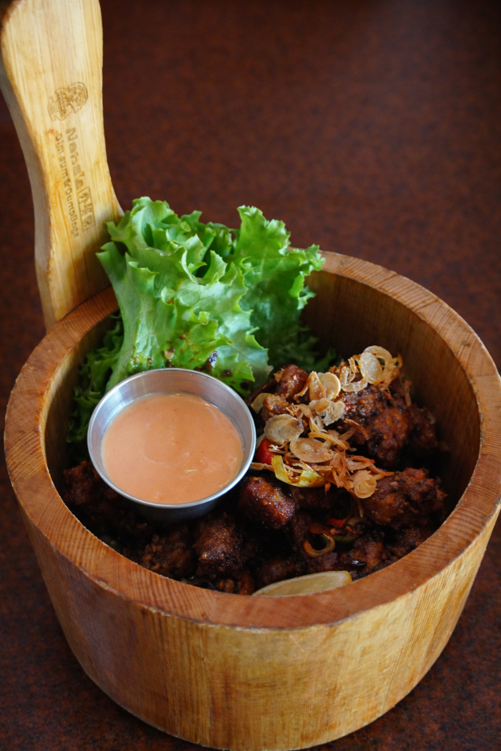 Spicy Chinese chicken in a wood bowl with dipping sauce for Nana's Dim Sum and Dumplings.