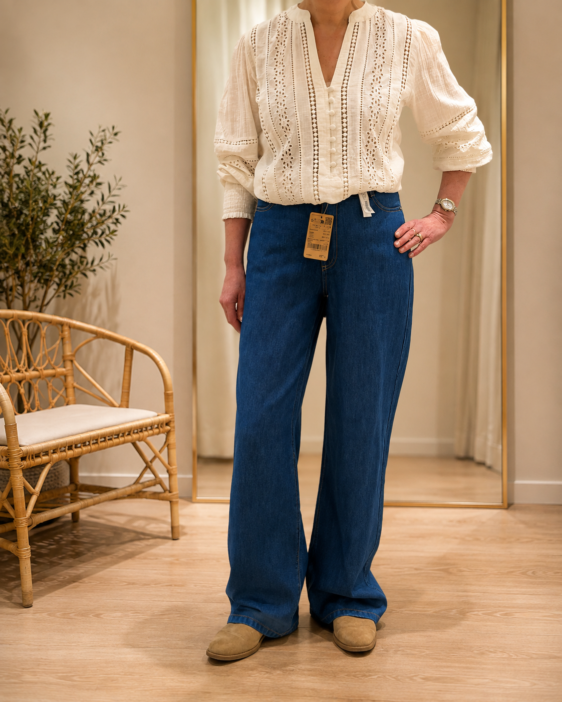 Vêtements d'une personne essayant une blouse beige avec broderies et pantalons en jean bleu dans un magasin de vêtements.