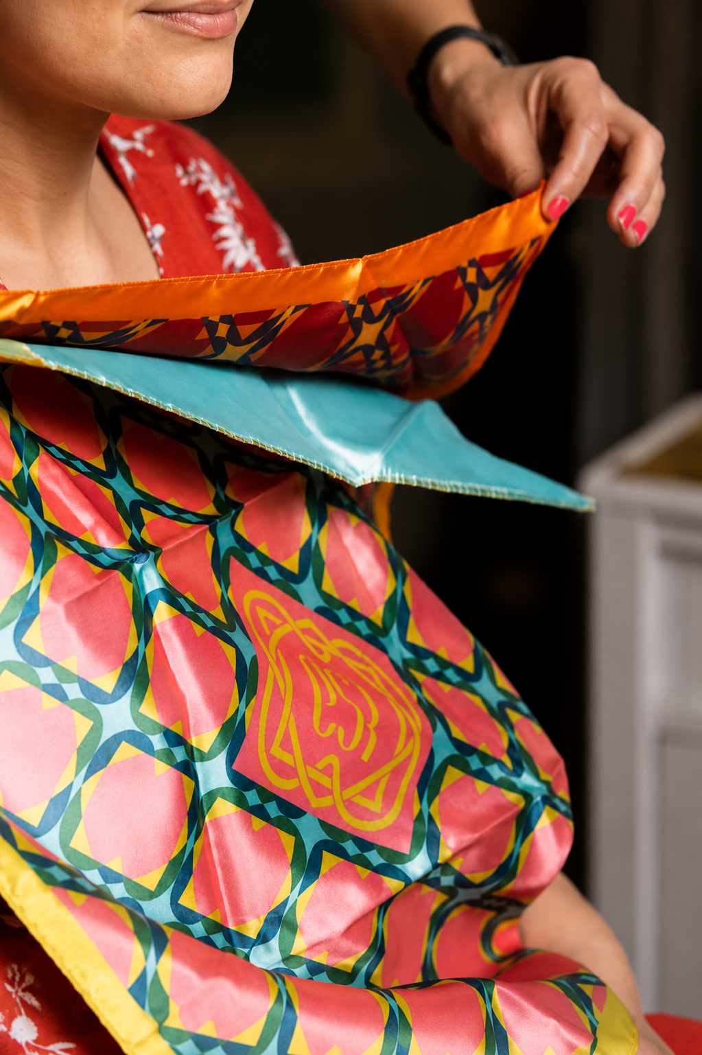 Une femme portant un tissu coloré avec des motifs géométriques et un logo, probablement lors d'une cérémonie ou d'un événement culturel.