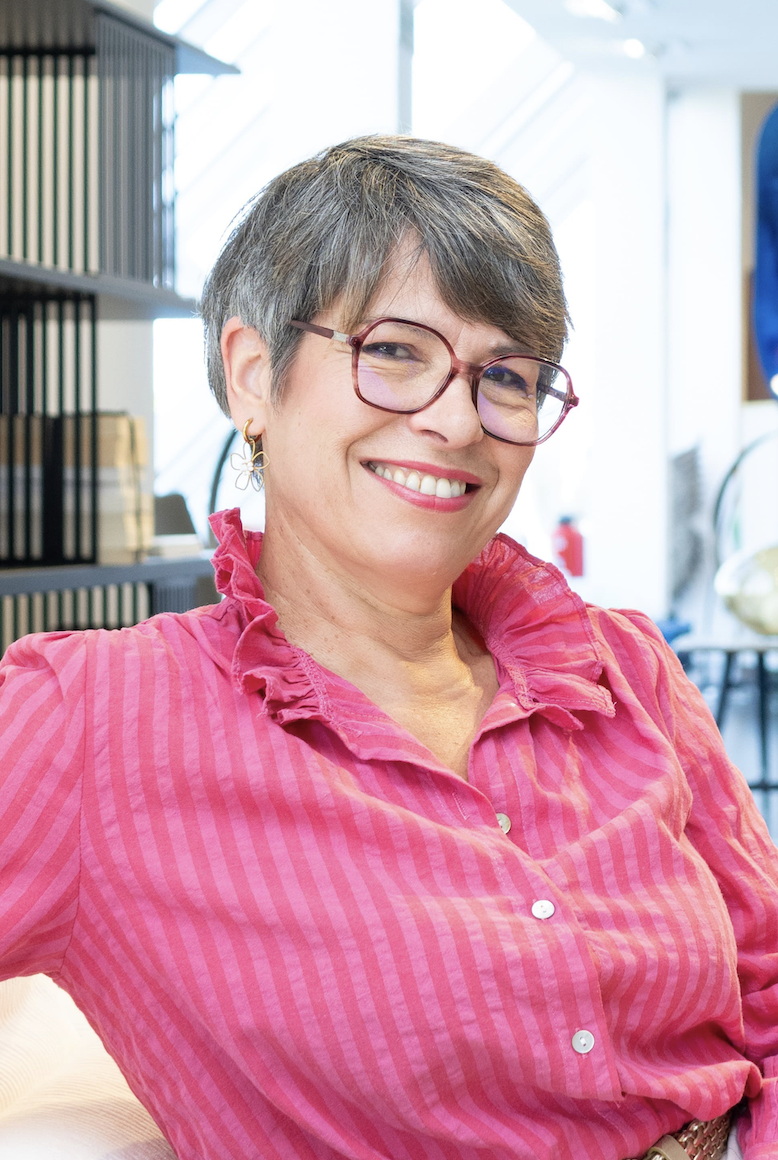 Femme souriante portant des lunettes roses et une chemise rose à rayures.