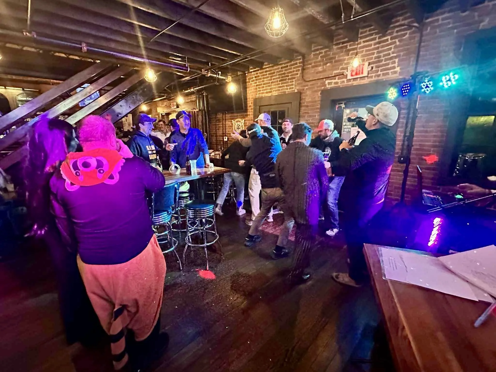 People socializing in a dimly lit bar with exposed brick walls and warm yellow lighting.