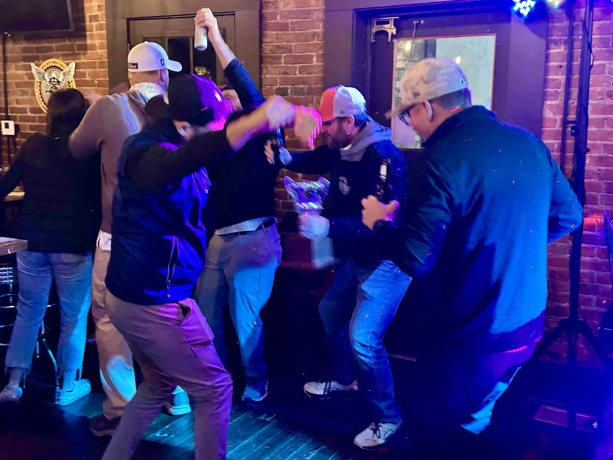 Group of people dancing and having fun at a party or celebration in a dimly lit venue with neon lighting and brick walls.