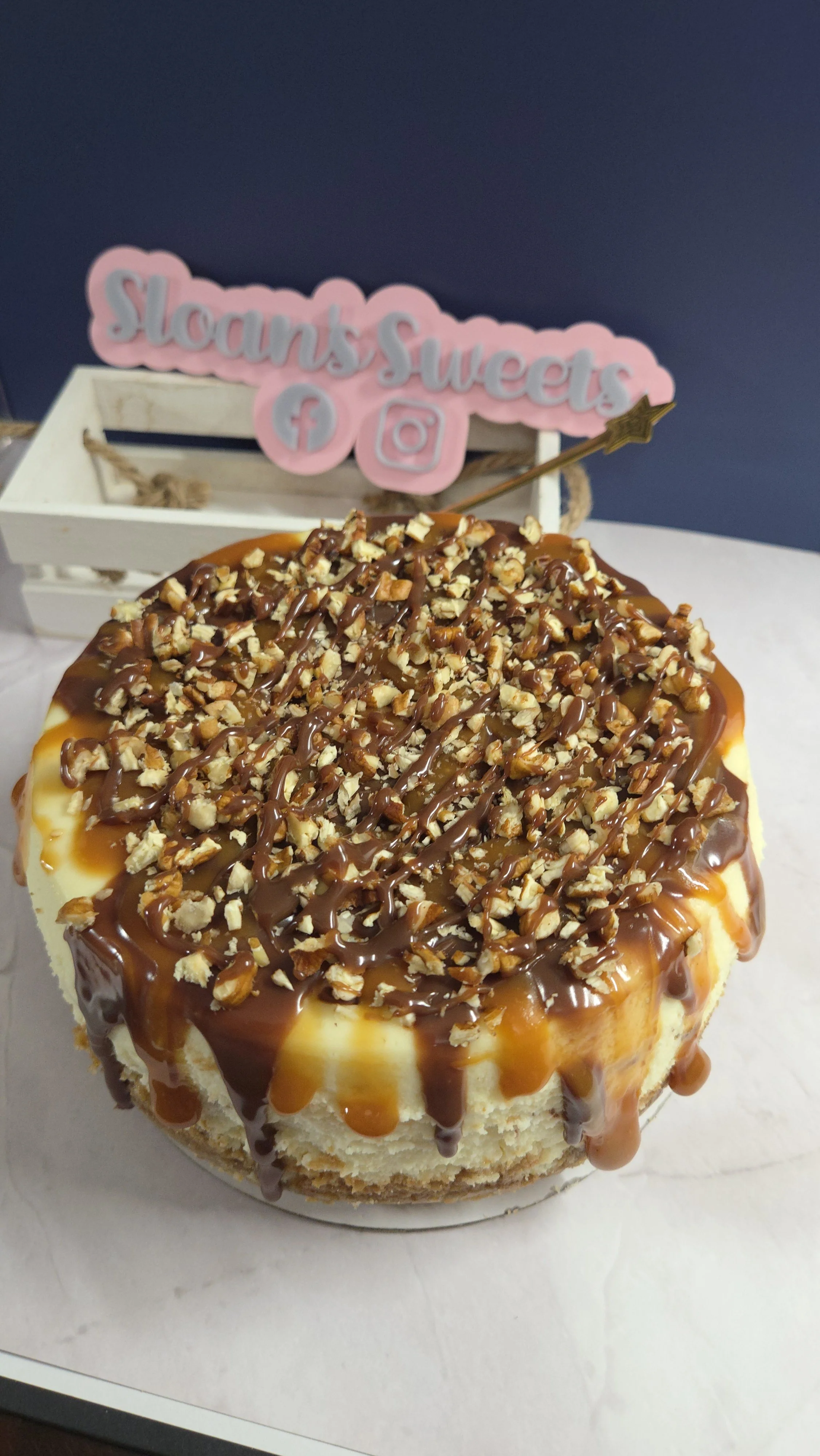 Gourmet New York style turtle cheesecake featuring a graham cracker crust, thick caramel and chocolate drips, and a heavy topping of chopped pecans, scratch-made at Sloan's Sweets and Sammies in Myrtle Beach.