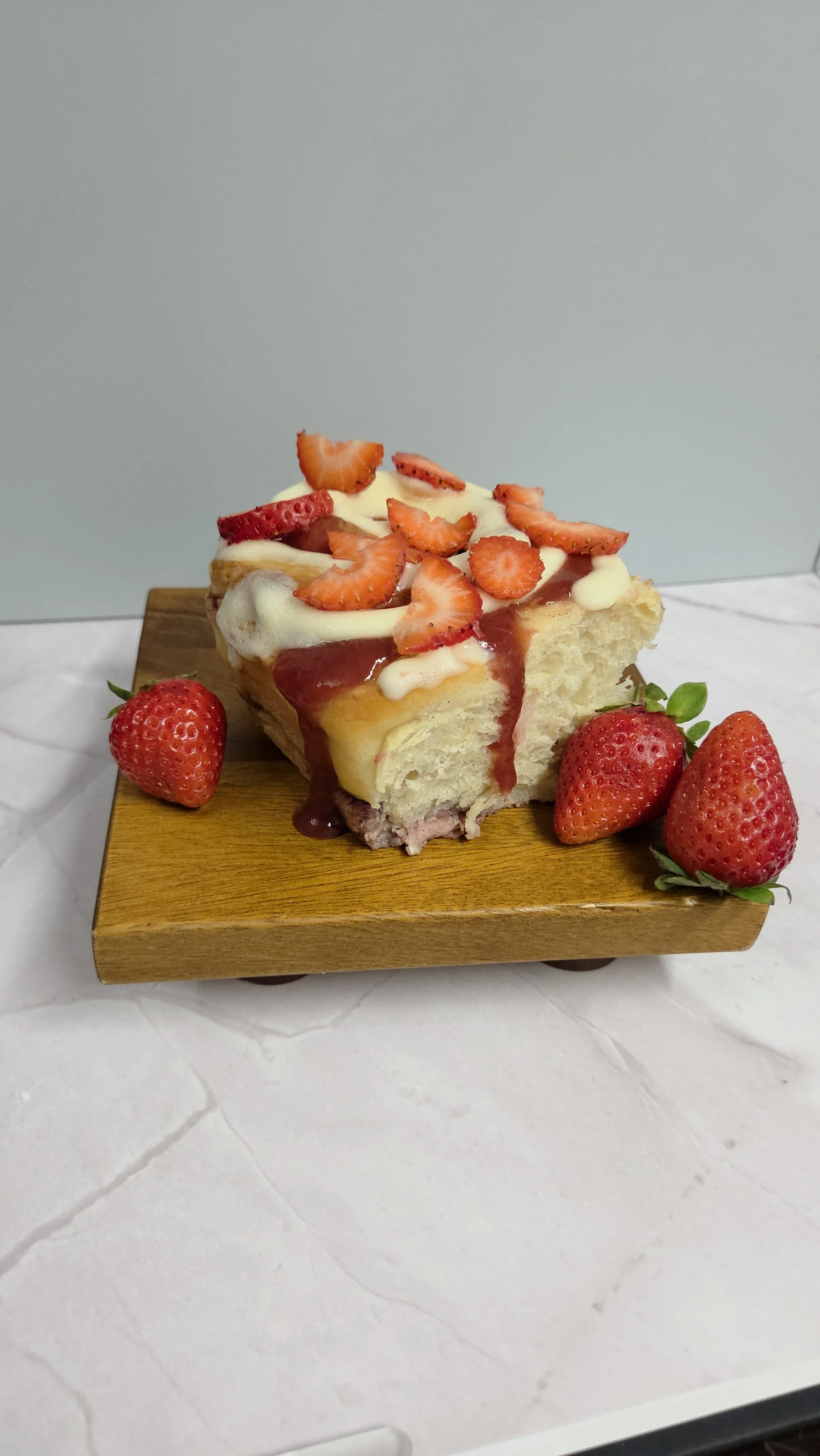 Gourmet strawberry cheesecake roll topped with buttercream icing, sweet strawberry glaze drizzle, and fresh sliced strawberries, baked scratch-made at Sloan's Sweets and Sammies in Myrtle Beach.