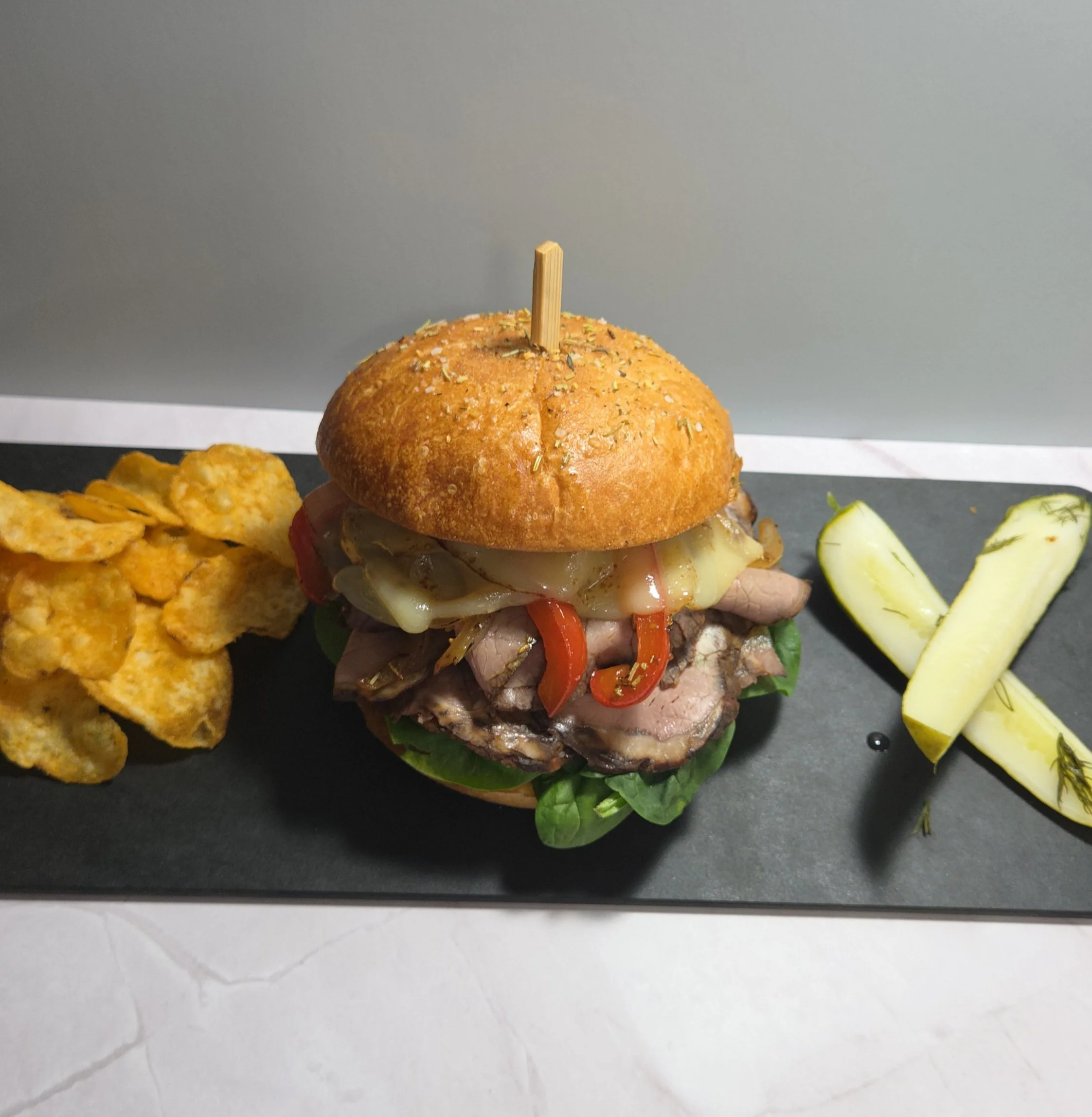 Gourmet roast beef sandwich with melted Swiss cheese, roasted red peppers, and fresh greens on a seasoned brioche bun, served with local potato chips and dill pickle spears at Sloan's Sweets and Sammies in Myrtle Beach. 