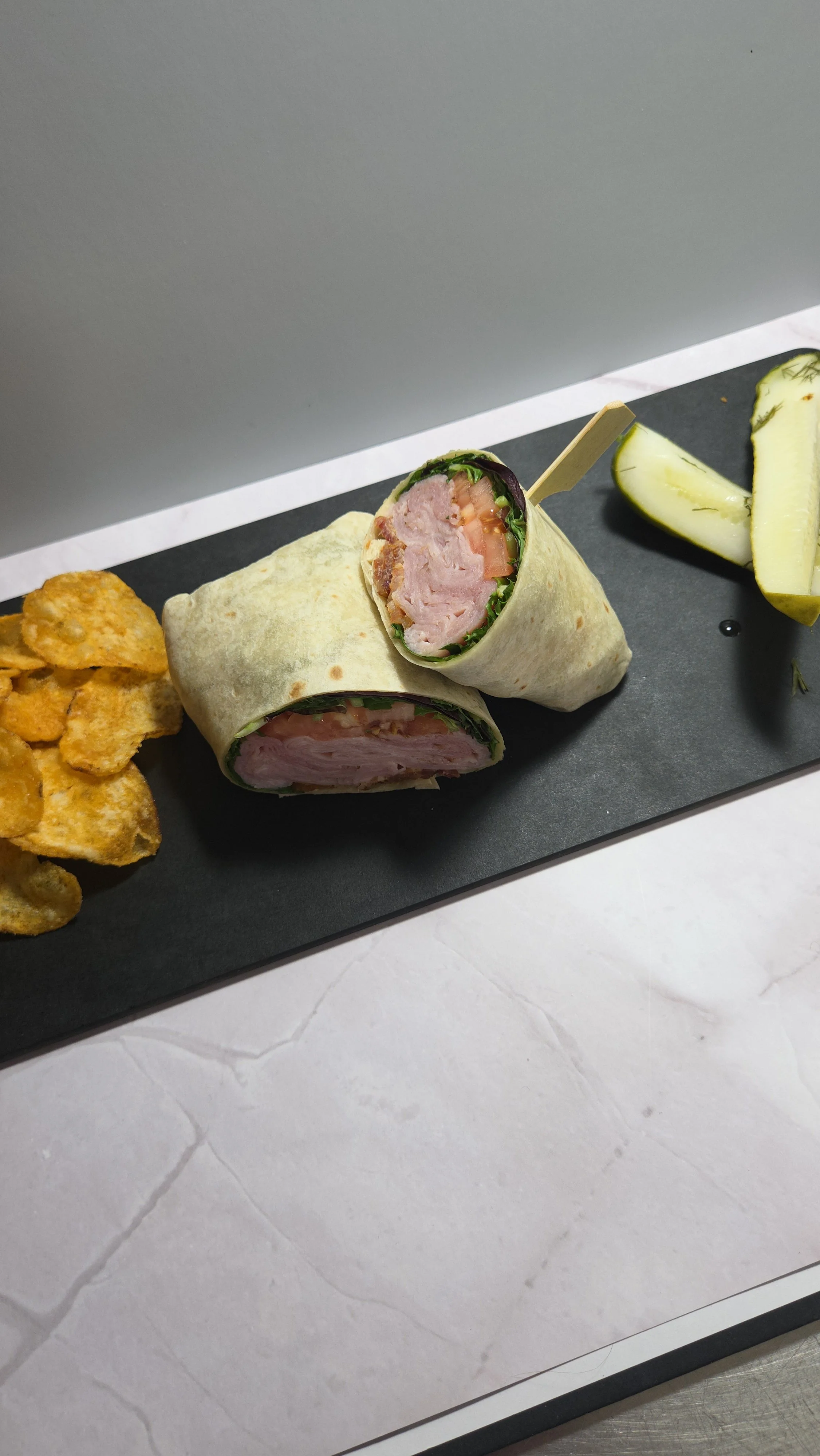 Gourmet ham and cheese lunch wrap with crisp lettuce, fresh tomatoes, and bacon in a flour tortilla, served with local potato chips and dill pickle spear at Sloan's Sweets and Sammies in Myrtle Beach.