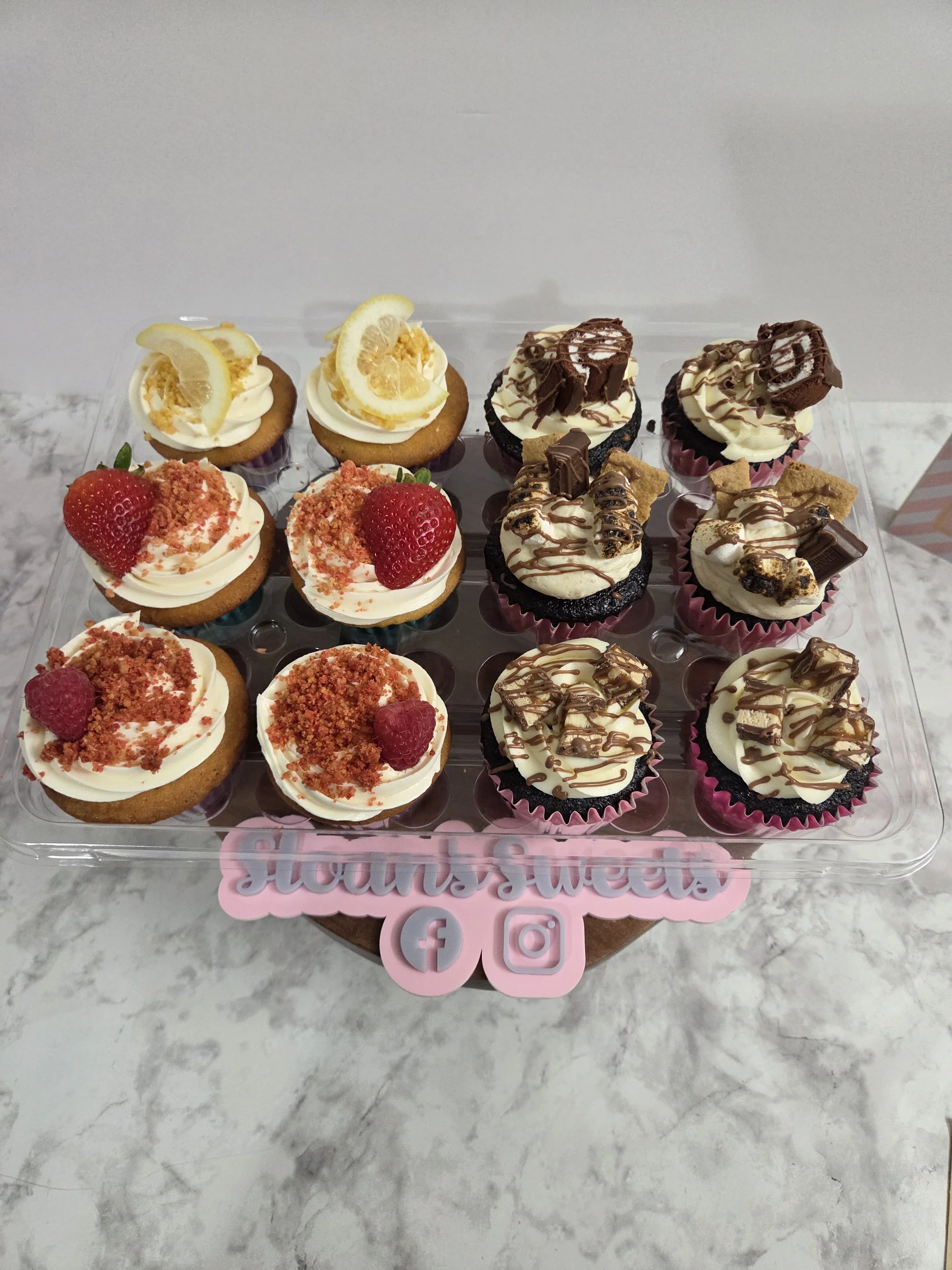 Gourmet assortment of custom cupcakes featuring lemon drop, strawberry crunch, raspberry, chocolate swiss roll, s'mores, and candy toppings, scratch-made by Sloan's Sweets and Sammies in Myrtle Beach.