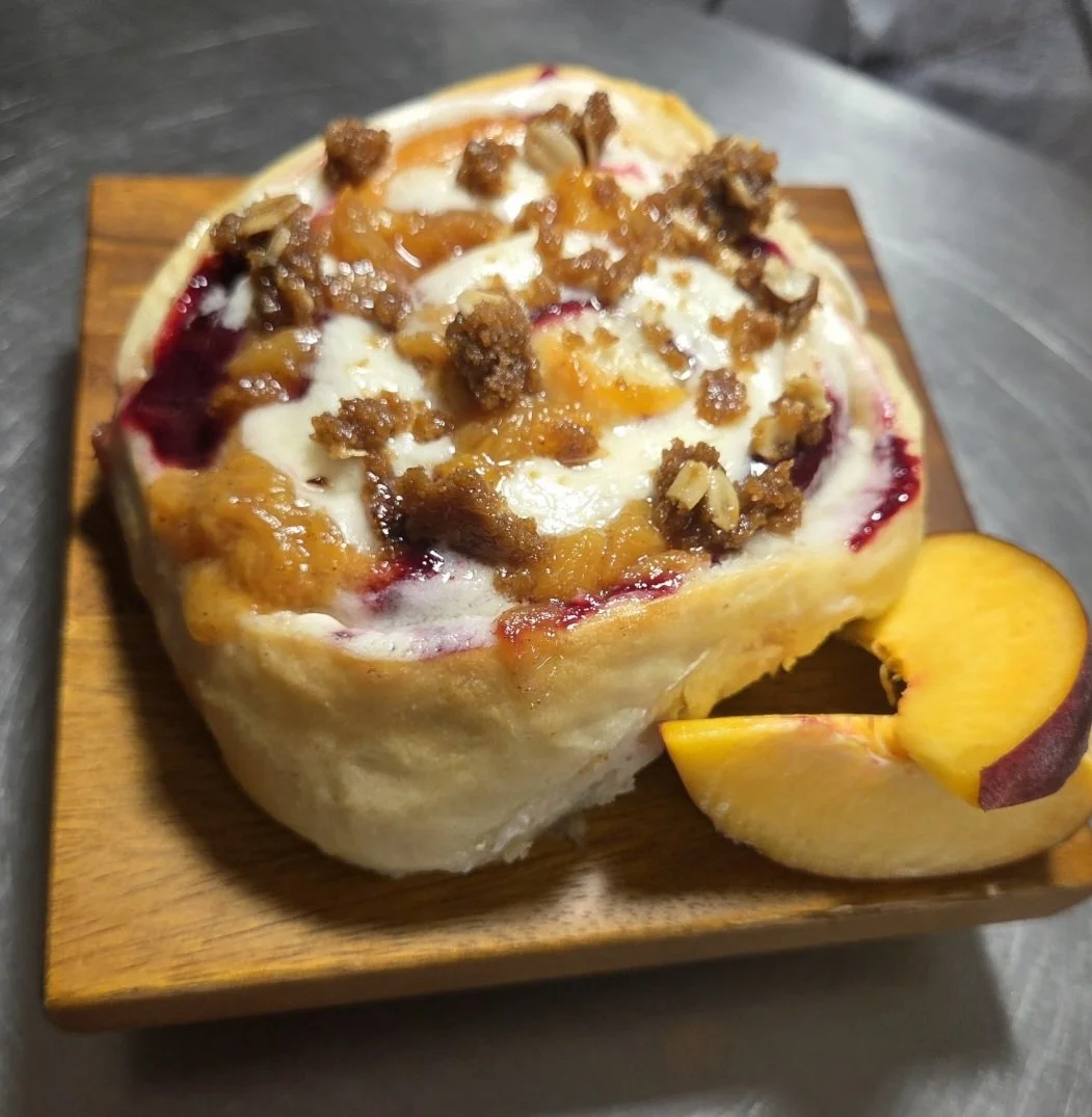 Gourmet peach and blackberry sweet roll with buttercream icing, brown sugar crumble topping, and fresh peach slices, baked scratch-made at Sloan's Sweets and Sammies in Myrtle Beach.