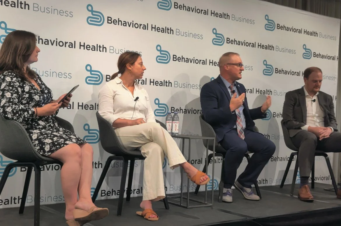 Four people seated on a stage during a panel discussion with a backdrop displaying "Behavioral Health Business" and a logo.