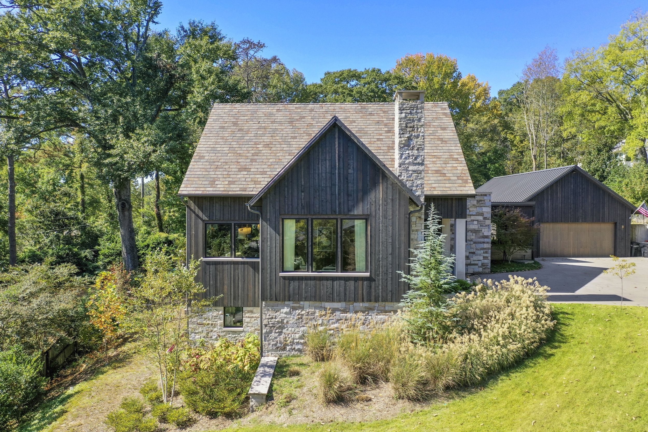 This custom home in Mountain Brook blends modern and traditional elements through a mix of stone, concrete, steel, and stained multi-plank wood siding. Custom steel awnings and textured concrete columns add character, while outdoor spaces and natural