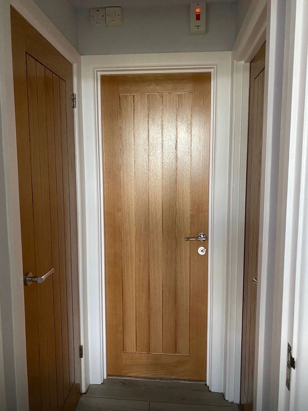 Indoor hallway with wooden doors on both sides and a central wooden door, white trim, and a gray floor.