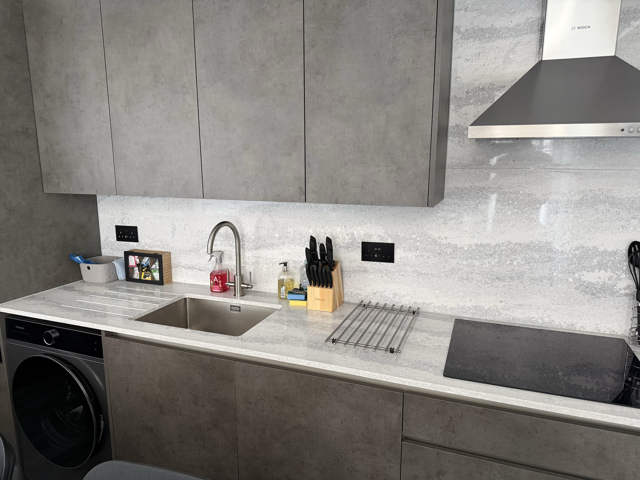 Modern kitchen with grey cabinetry, a white countertop, a sink, a stovetop, a microwave, and various kitchen accessories.
